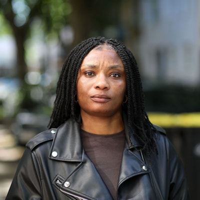 Janefrancis Kalu aus Nigeria im Porträt. Sie trägt ihre schwarzen Haare lang und eine schwarze Lederjacke mit braunem T-Shirt.