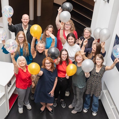 Frauen und ein Mann halten Luftballons in die Höhe. Sie freuen sich.