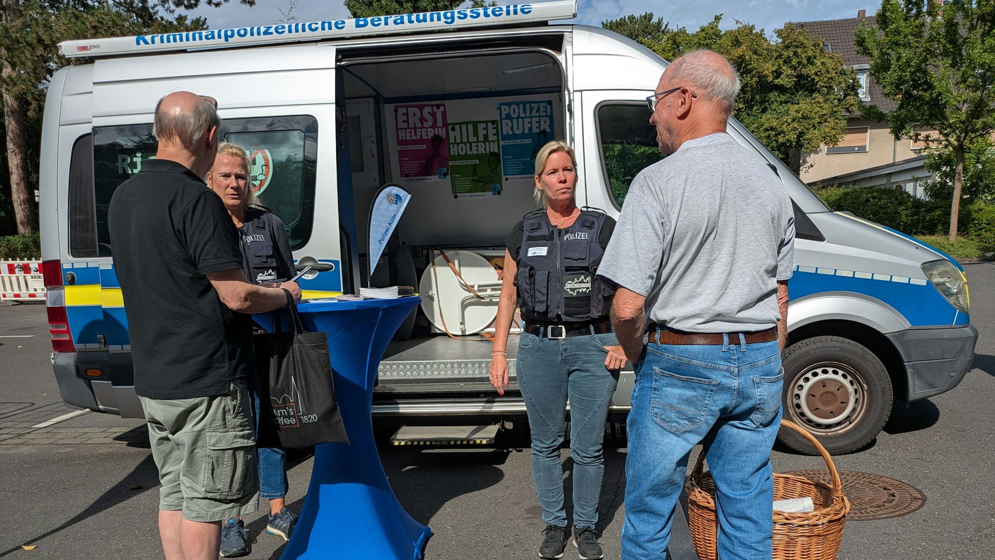 Zwei Polizistinnen und zwei Männer unterhalten sich vor einem Fahrzeug der Polizei.