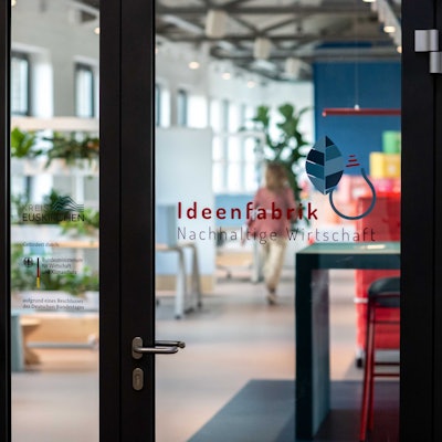 Auf einer Glastür ist die Aufschrift „Ideenfabrik Nachhaltige Wirtschaft“ aufgeklebt