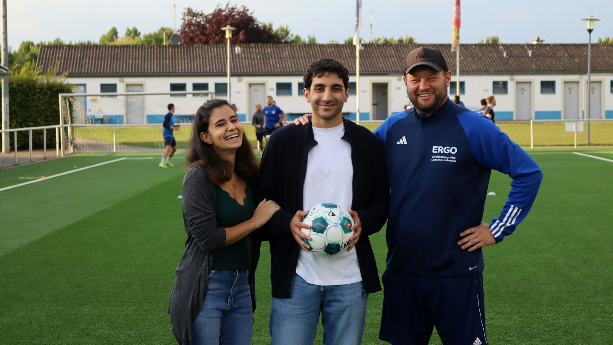 Patrick Hinsch hält einen Ball in der Hand, seine Freundin und sein Trainer halten ihn im Arm.