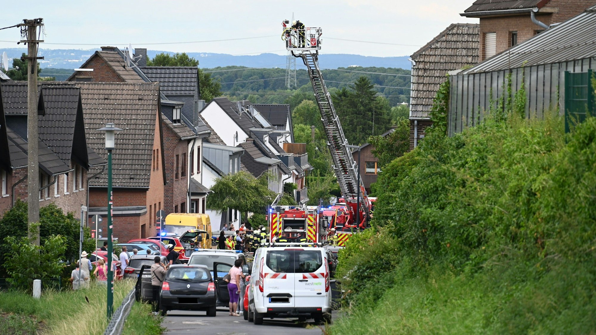 Das Bild zeigt eine Straße mit mehreren Feuerwehrfahrzeugen und Nachbarn.