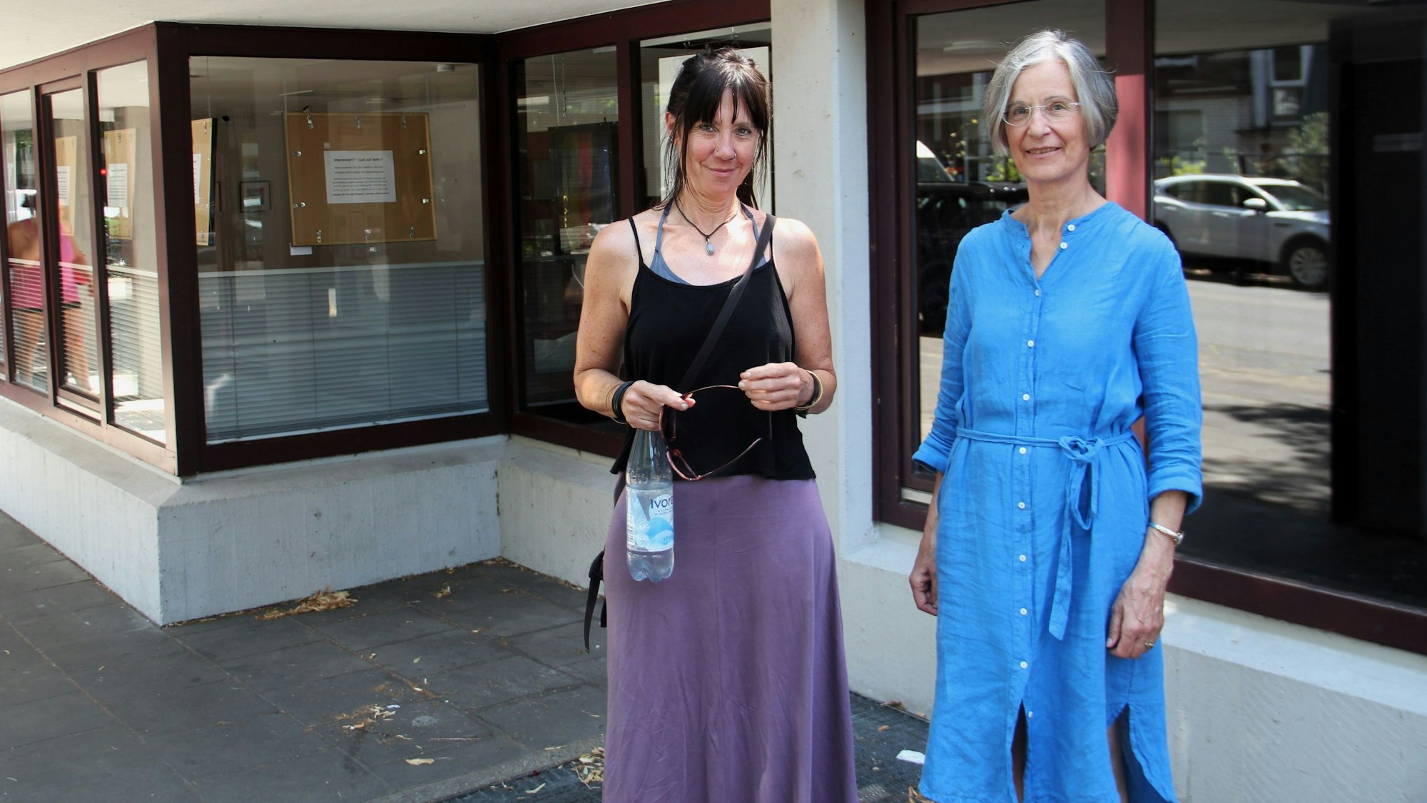 Zwei Frauen stehen vor einem Gebäude mit großen Fenstern.