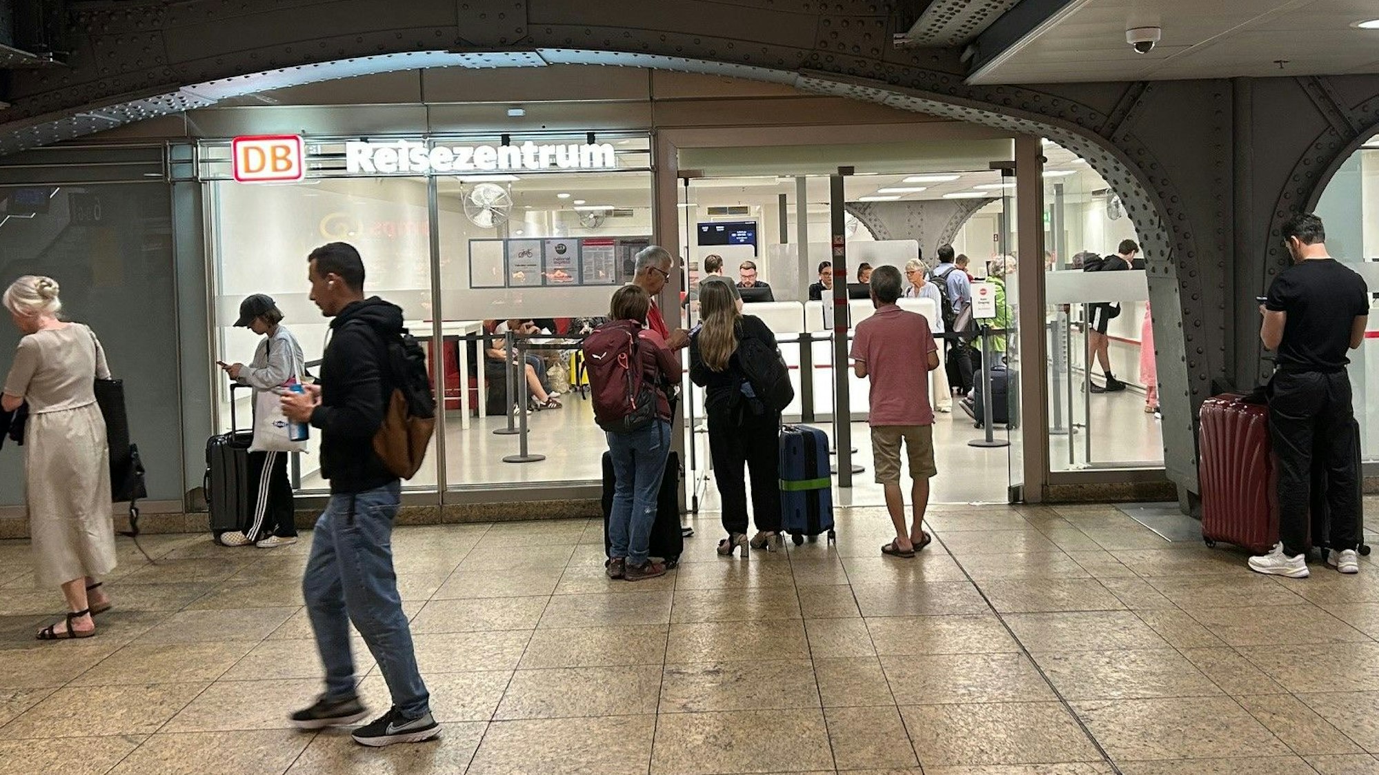 Bahnkunden warten vor dem provisorischen Reisezentrum im Kölner Hauptbahnhof zwischen den Gleisen 5 und 6. Das alte Reisezentrum wird modernisiert und soll laut DB im ersten Quartal 2026 wieder eröffnen. Foto: Peter Berger