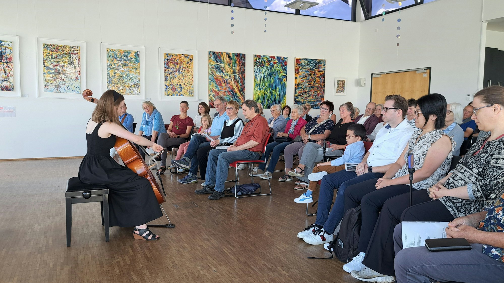Das Foto zeigt die Cellistin Emma Gilbert vor Publikum. Im Hintergrudn sind Ölbilder von Uwe Gieschen zu sehen