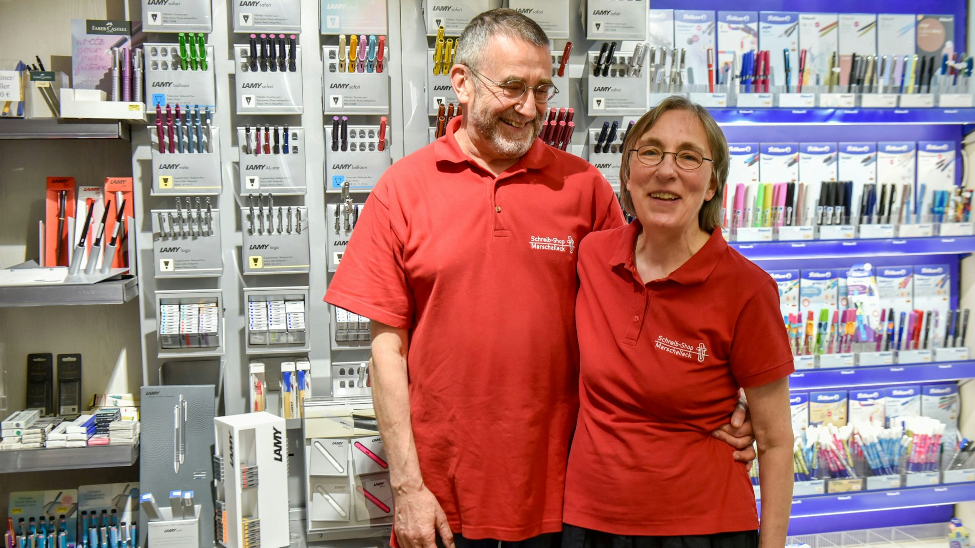 Eine Frau und ein Mann in roten Polohemden stehen vor einer Wand mit Stiften.