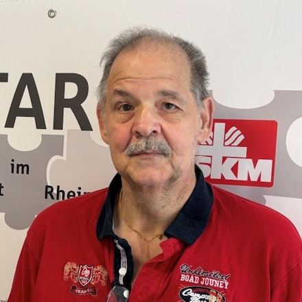Auf dem Bild ist das Portrait eines Mannes zu sehen, er trägt ein rotes Poloshirt.