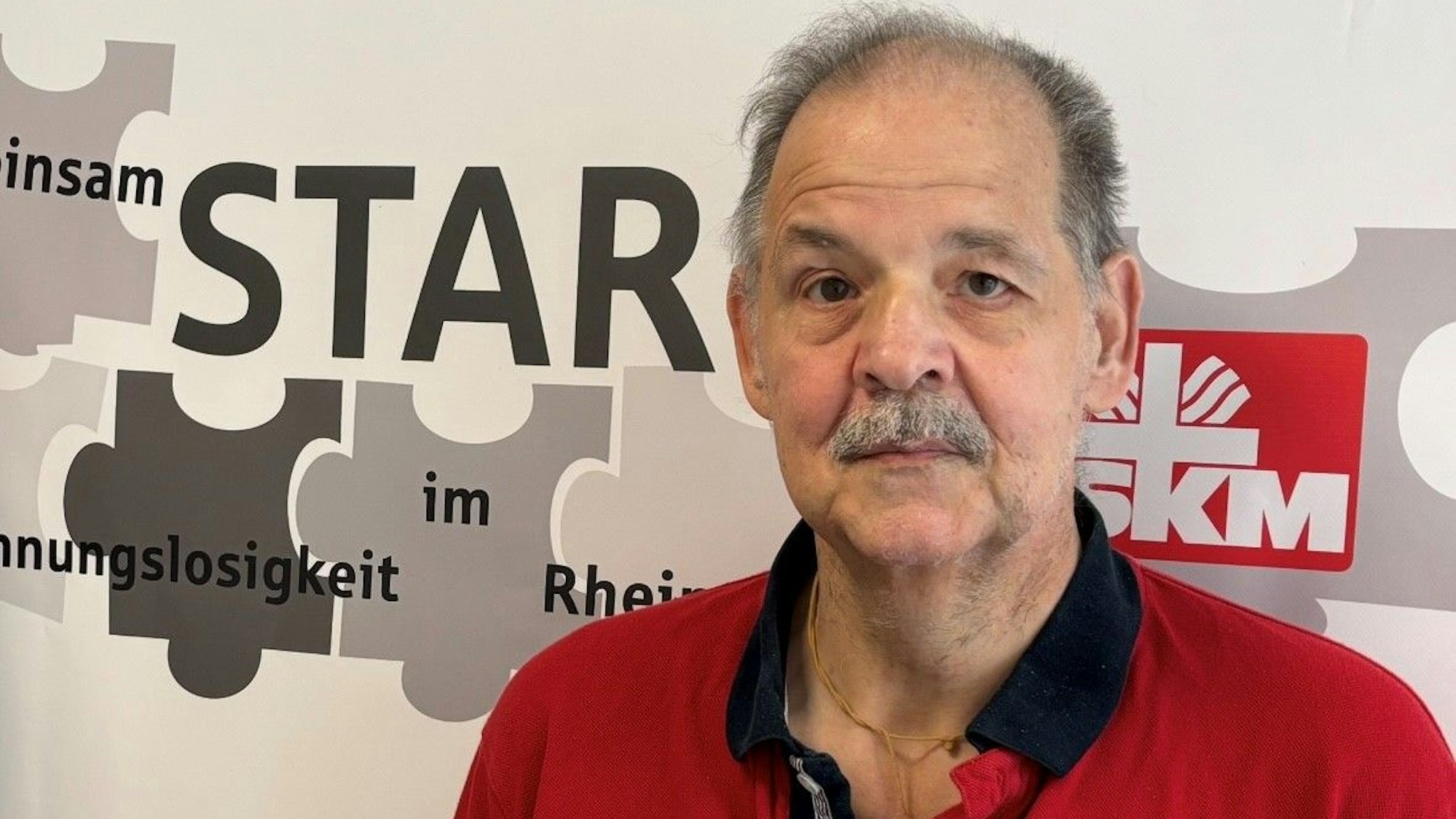 Auf dem Bild ist das Portrait eines Mannes zu sehen, er trägt ein rotes Poloshirt.