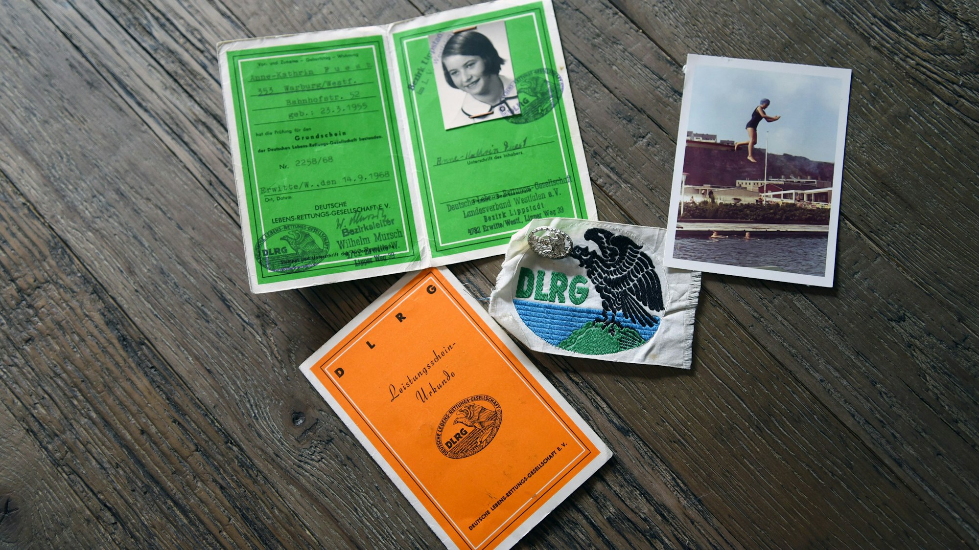 Zwei Schwimmabzeichen und ein Bild von Anne-Kathrin von früher, wie sie von einem Sprungturm springt, liegen auf einem Tisch.
