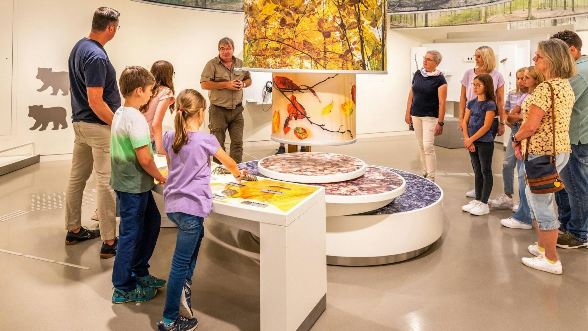 Ein Ranger steht an einer Station und erklärt Kindern und Erwachsene die Ausstellung.