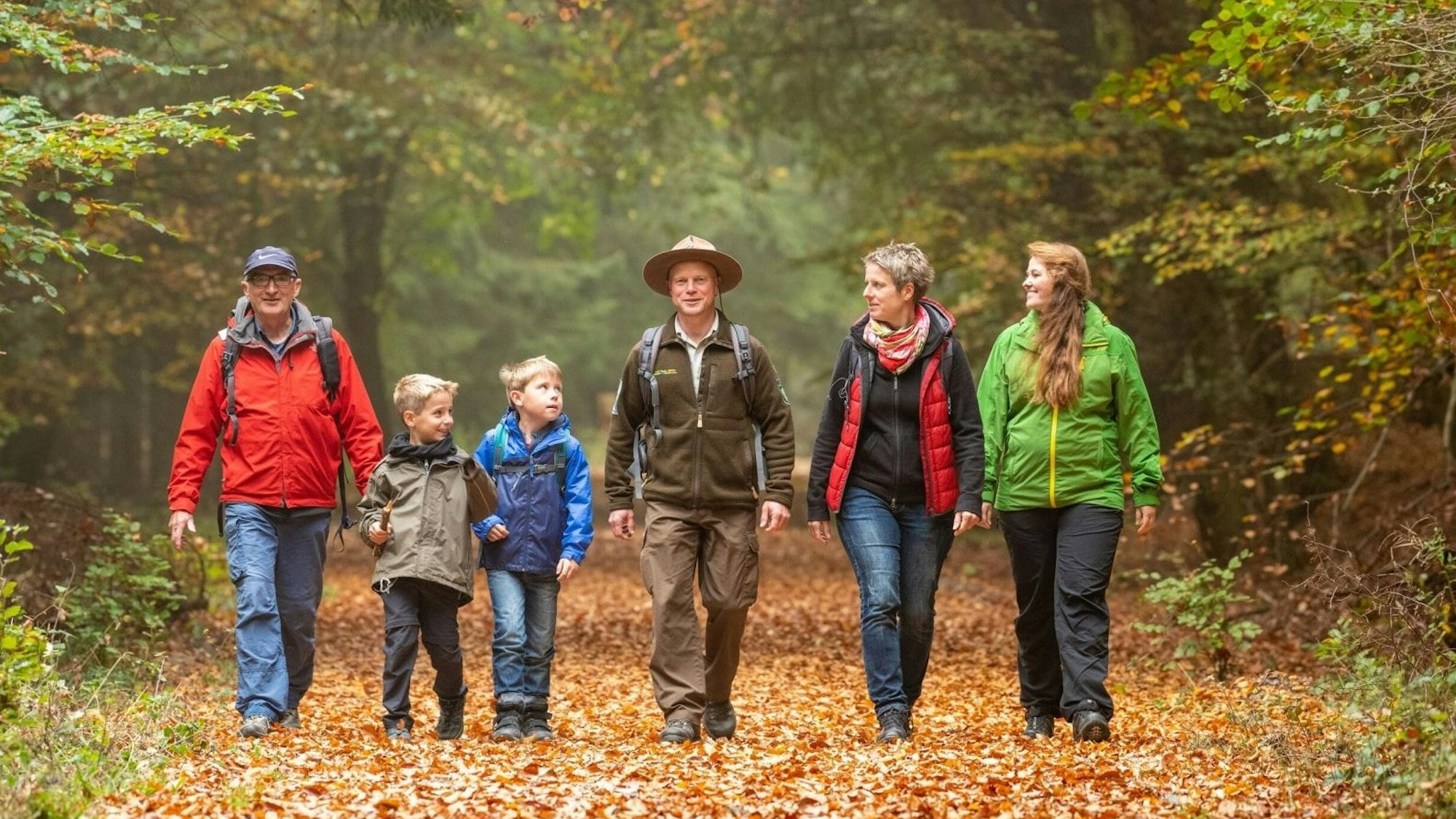 Ein Ranger geht inmitten einer Gruppe von drei Erwachsenen und zwei Kindern durch den Wald.