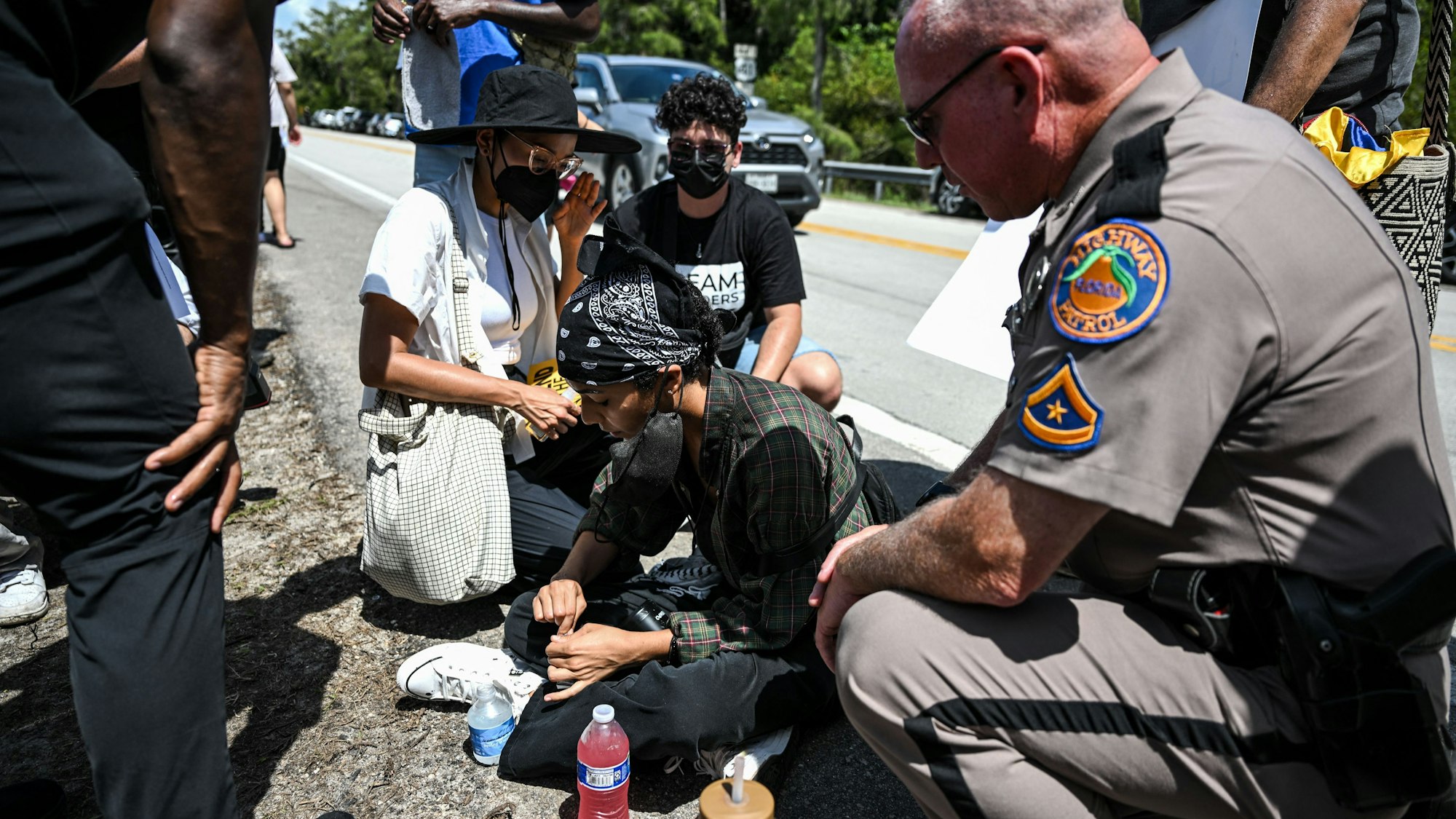 Demonstranten und ein Beamter der Florida Highway Patrol helfen einer Frau, die aufgrund der Hitze zusammengebrochen ist, als sie an einer Demonstration gegen die Schließung eines Einwanderergefängnisses in den Everglades teilnahm.