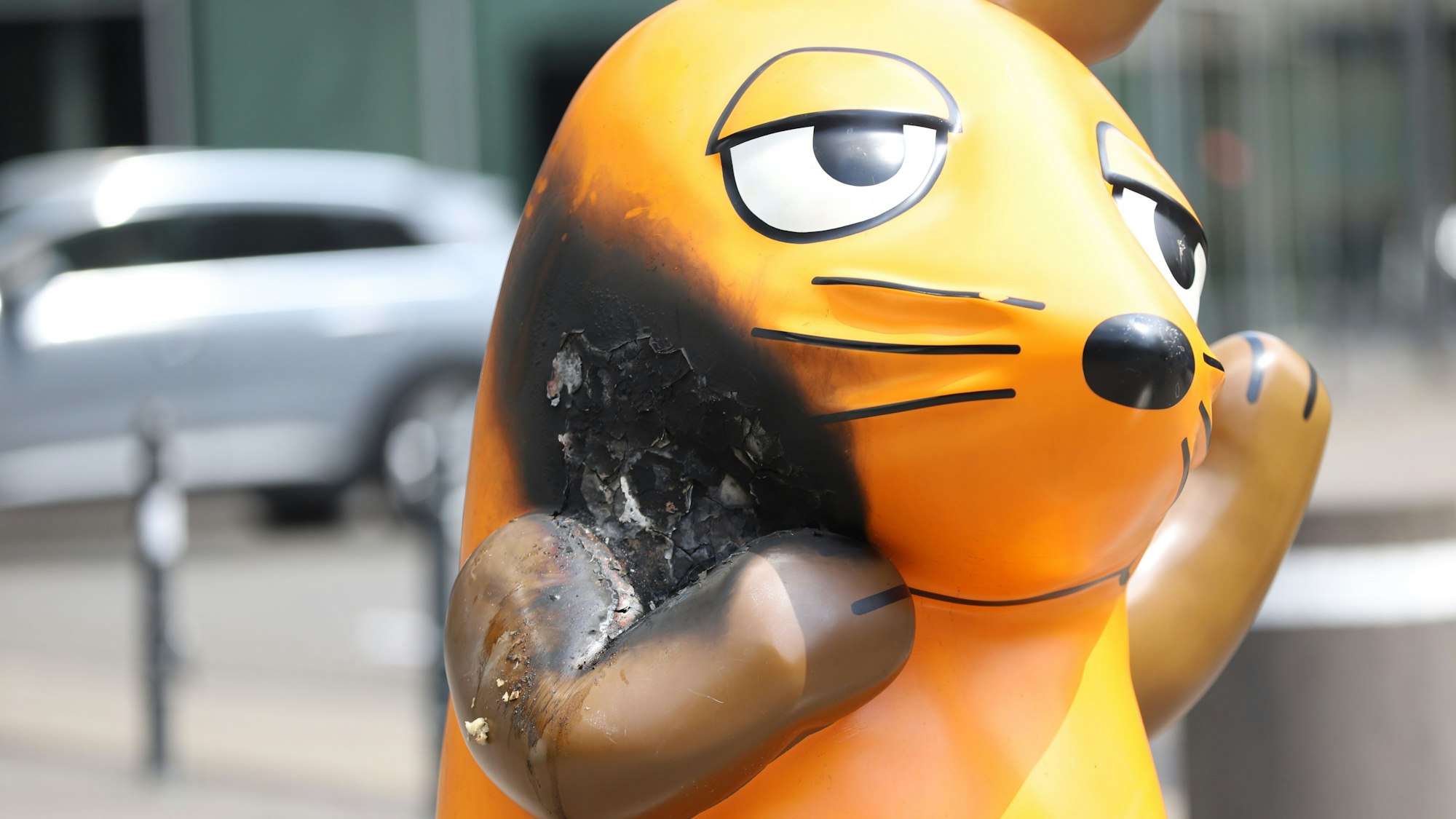 Mit einem großen Brandfleck steht die Maus vor dem WDR-Gebäude.