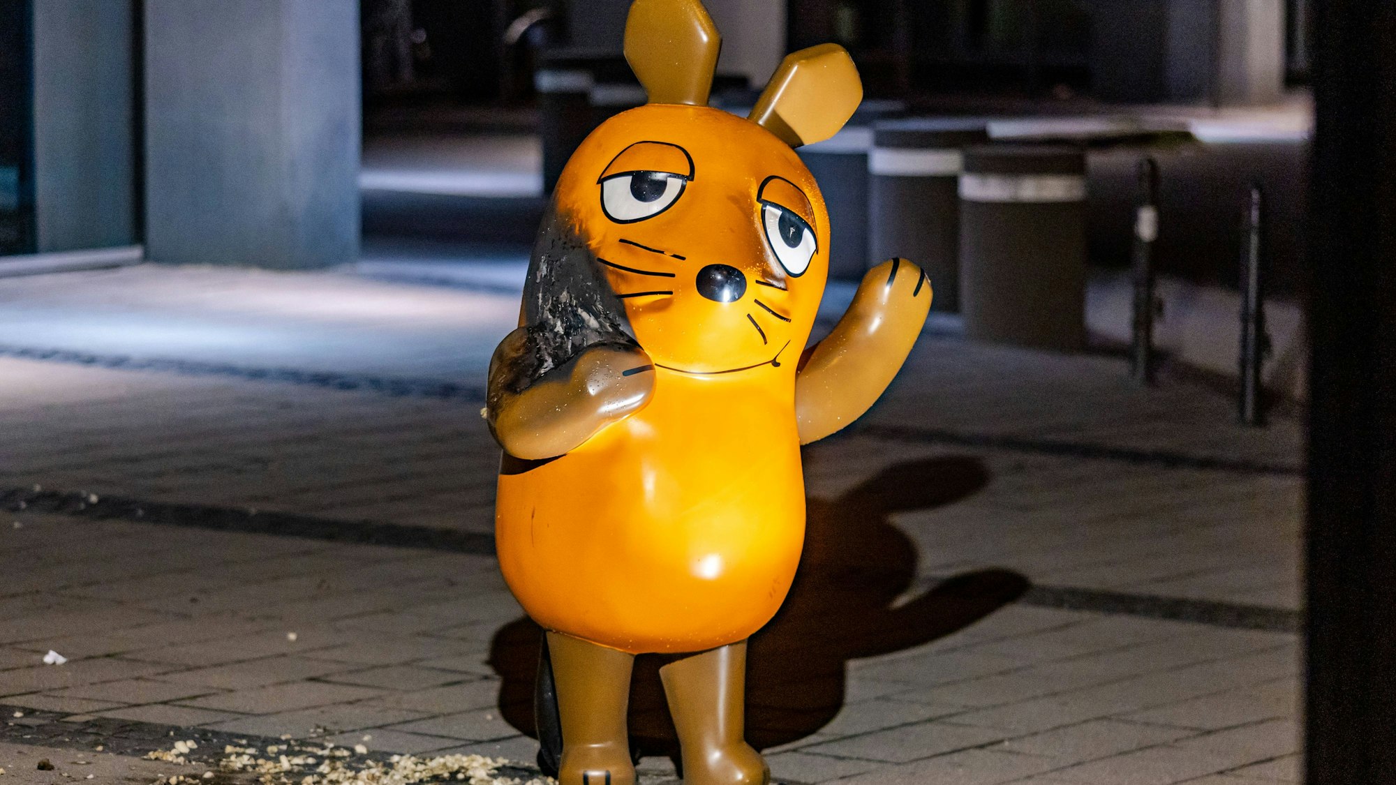 Maus Denkmal vor WDR Gebäude in Köln angezündet 27.07.2025 Das beschädigte Maus-Denkmal der Sendung mit der Maus steht einen Tag nach dem Brandanschlag vor dem WDR-Gebäude an der Mörsergasse in Köln. Die nächtliche Aufnahme zeigt die teils verbrannte Skulptur im Licht eines Spotlights, das einen langen Schatten wirft. Auf dem Boden liegen schwammartige Materialreste, die offenbar zum Entzünden des Feuers verwendet wurden. Die Feuerwehr konnte den Brand löschen, die Polizei ermittelt. Köln Innenstadt Nordrhein-Westfalen Deutschland *** Mouse monument in front of WDR building in Cologne set on fire 27 07 2025 The damaged Mouse monument from the show Sendung mit der Maus stands in front of the WDR building on Mörsergasse in Copyright: xBonn.digitalx/xMarcxJohnx