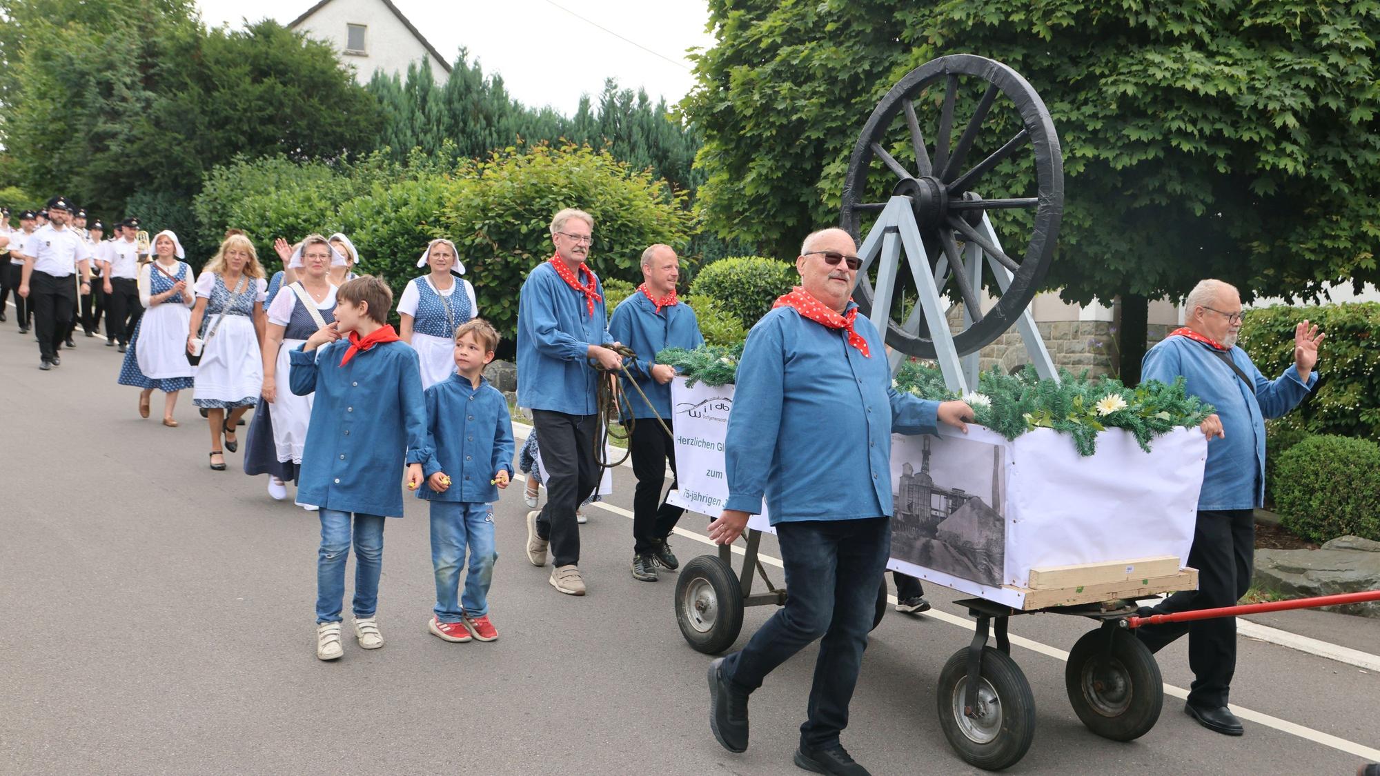 Viele Kinder und Erwachsene gehen auf einer Straße entlang. Mit dabei ein großer Bollerwagen.
