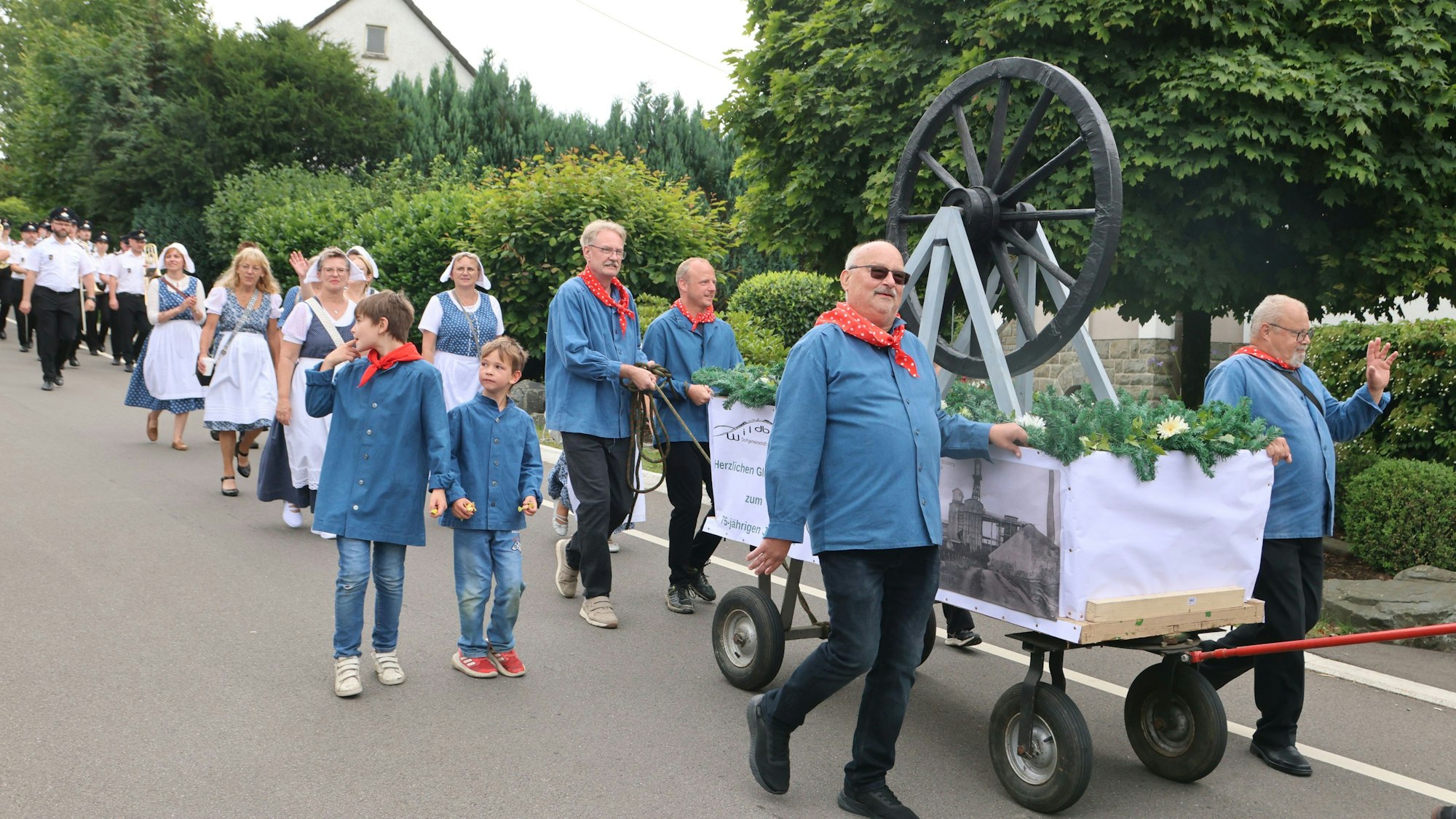 Viele Kinder und Erwachsene gehen auf einer Straße entlang. Mit dabei ein großer Bollerwagen.