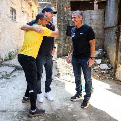 Favela-Einwohner Mineiro (l.) umarmt Bayer-04-Chef Fernando Carro. Daneben Jorginho.