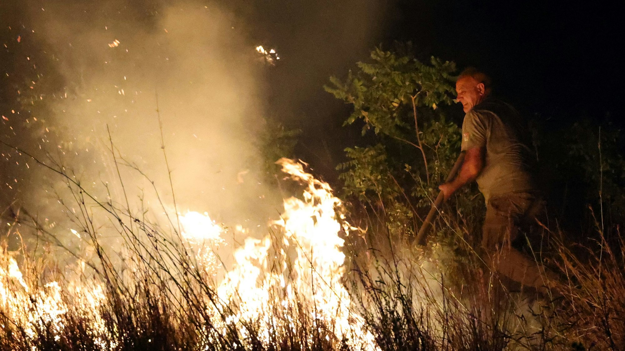 Ein Mann versucht in der Nacht, die Flammen eines Feuers einzudämmen.