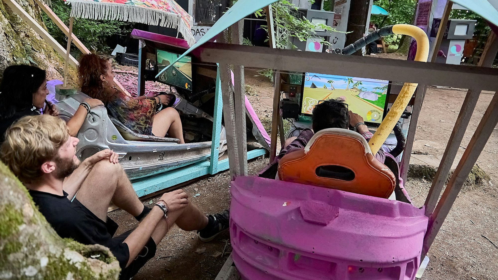 Junge Männer und Frauen sitzen in alten Autoscootern, vor sich haben sie einen Bildschirm.