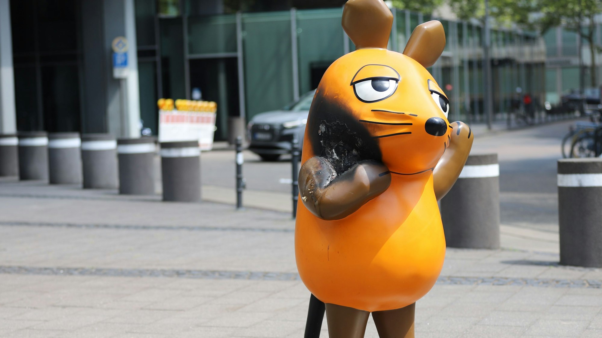 Die beschädigte Maus-Figur vor dem WDR-Gebäude in Köln mit einem großen Brandfleck.