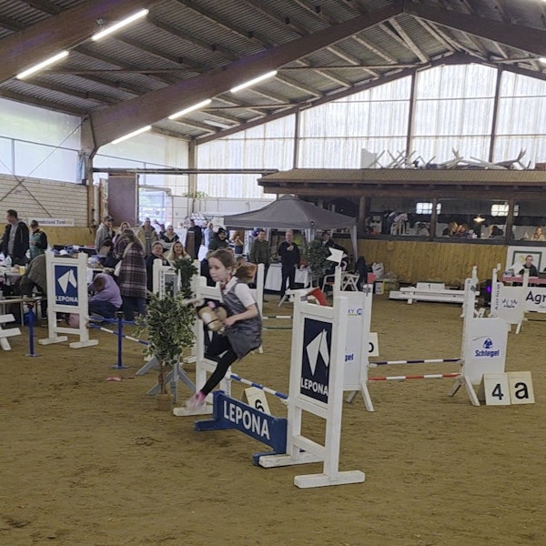 Ein Mädchen springt mit einem Steckenpferd über ein Hindernis.