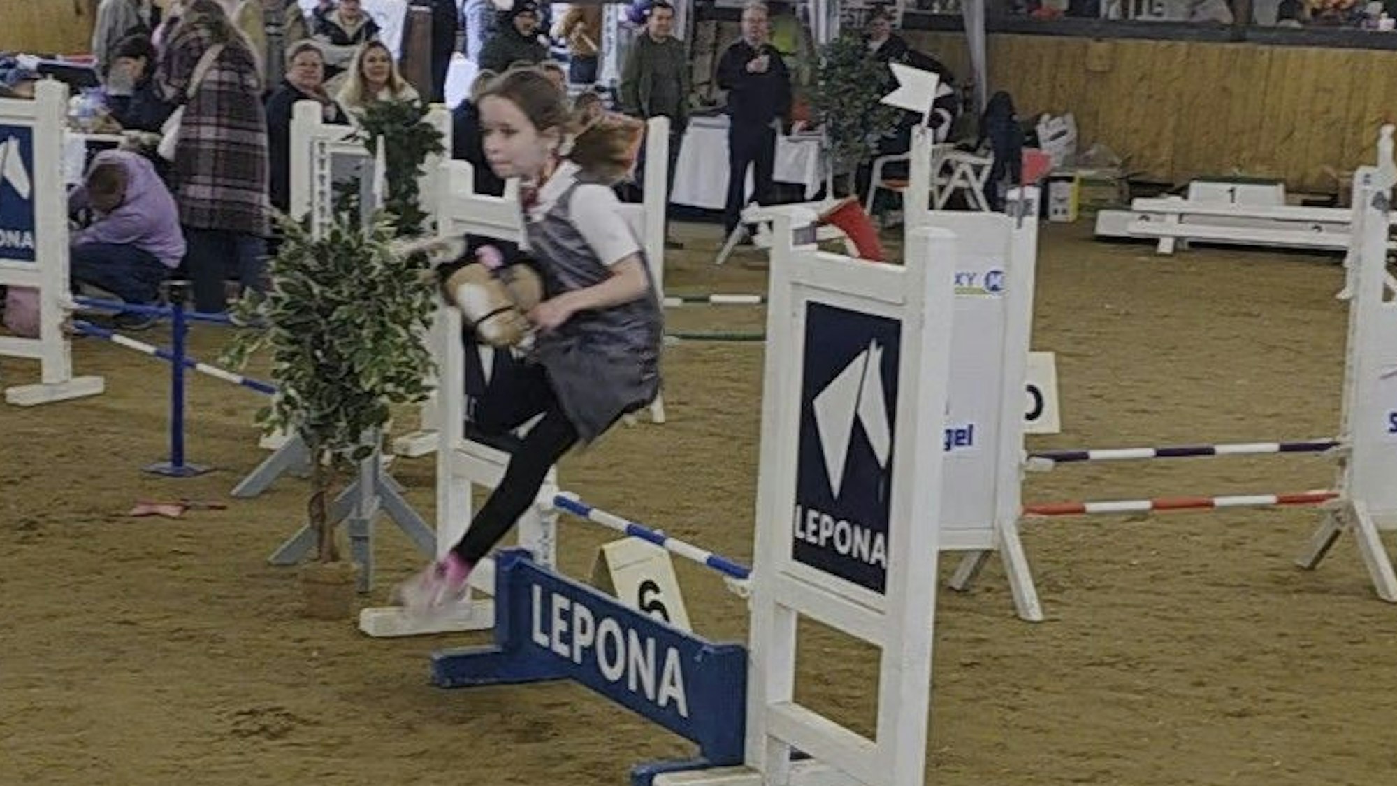 Ein Mädchen springt mit einem Steckenpferd über ein Hindernis.