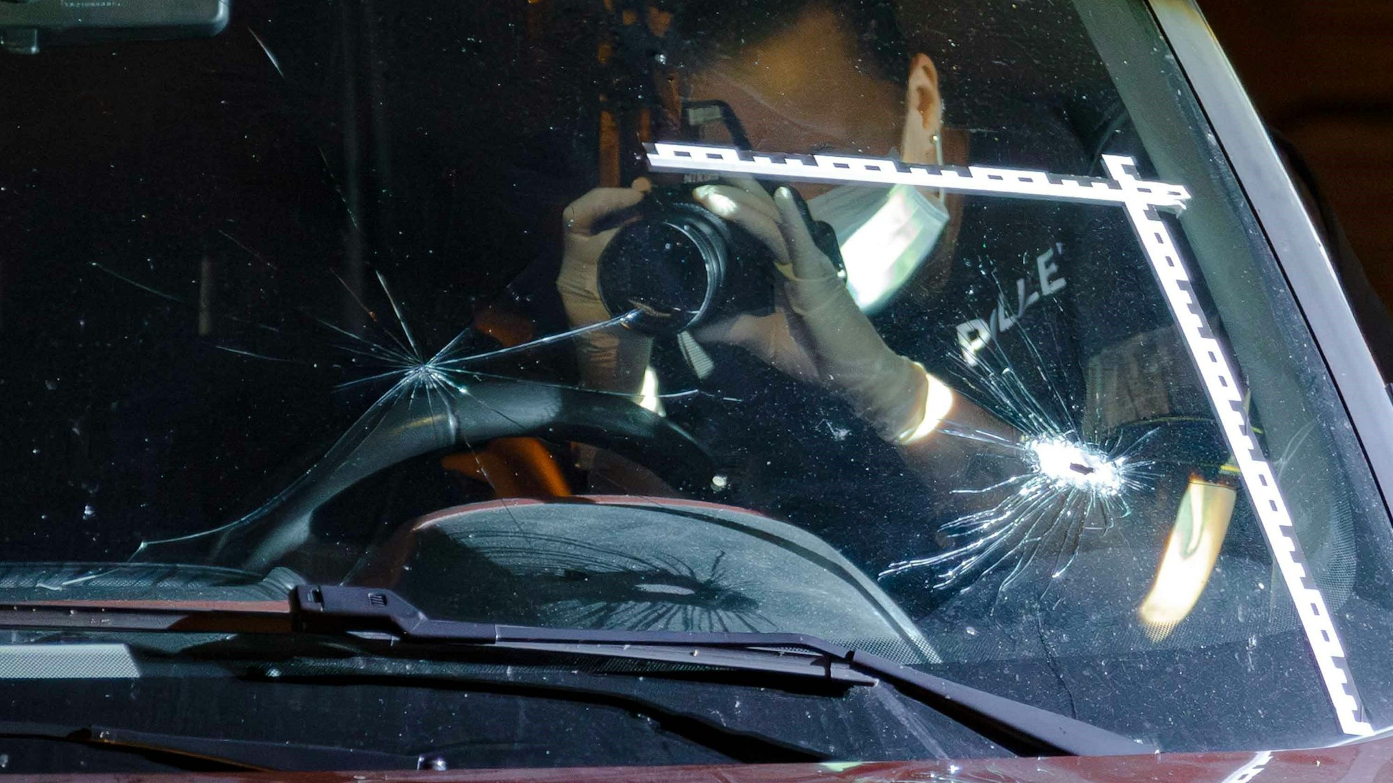 Schüsse in Holweide: Ein Polizeibeamter fotografiert Einschusslöcher in einer Windschutzscheibe.