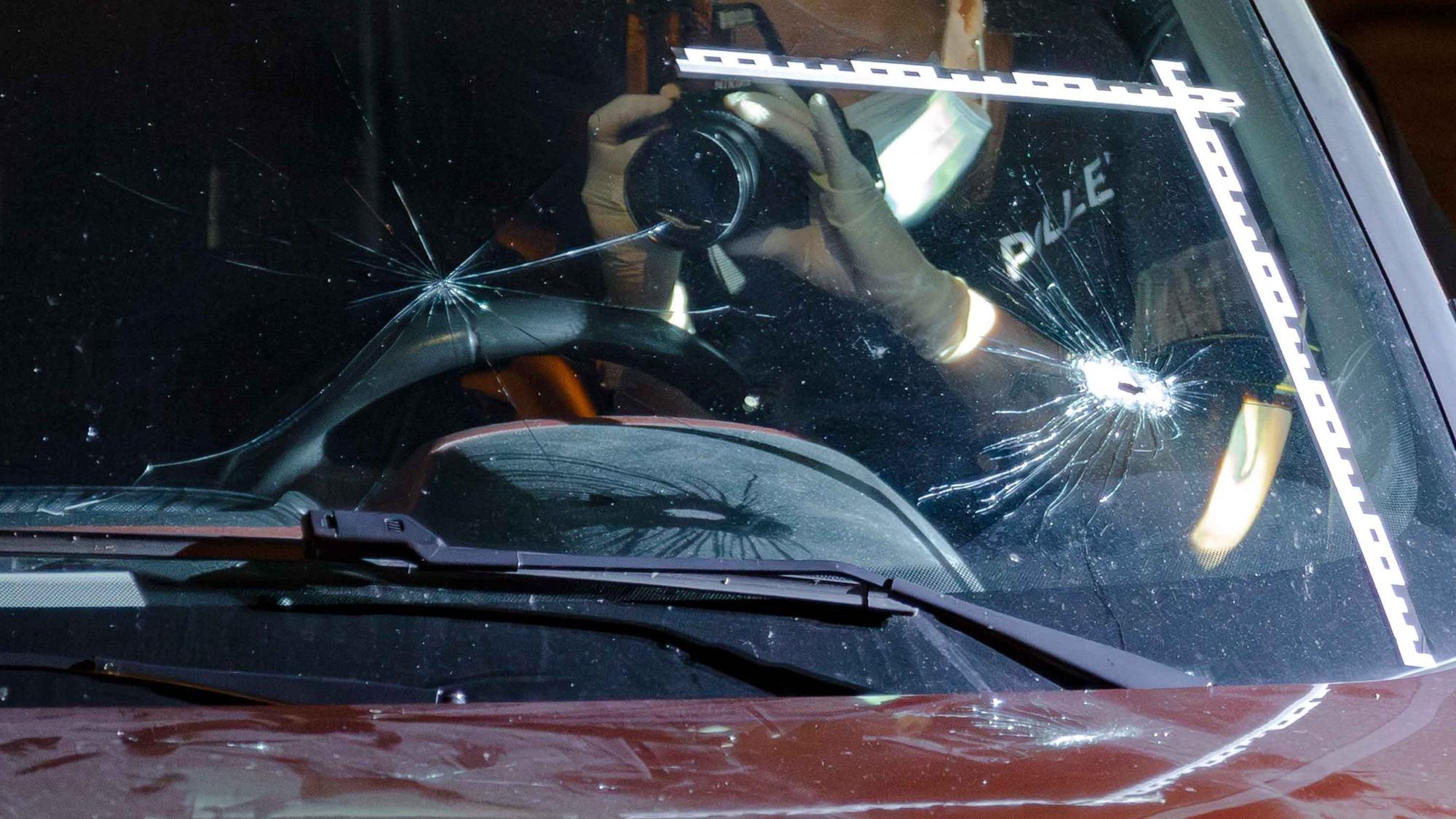 Ein Polizeibeamter fotografiert Einschusslöcher in einer Windschutzscheibe.