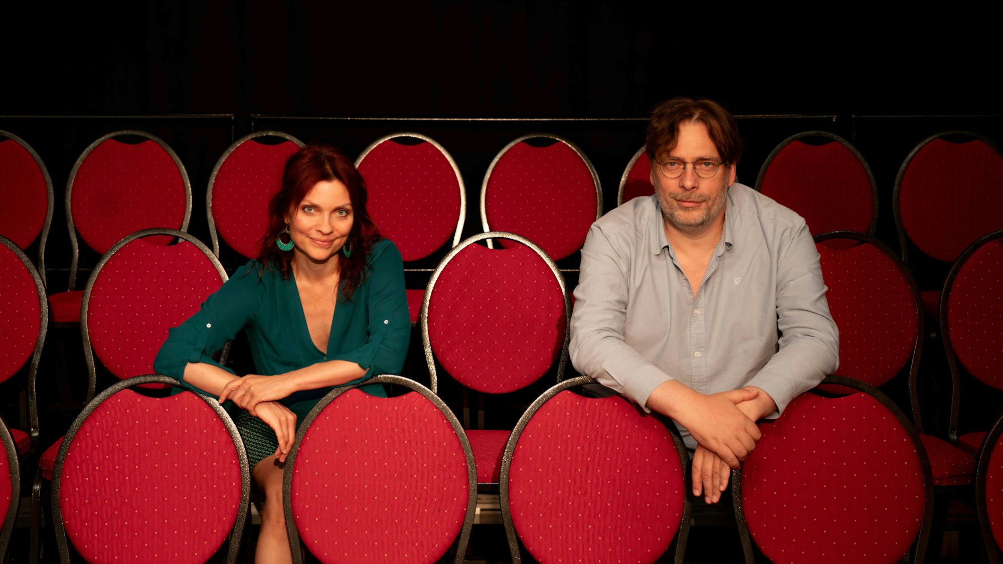 Eine Frau und ein Mann sitzen auf den roten Stühlen eines Theatersaals.