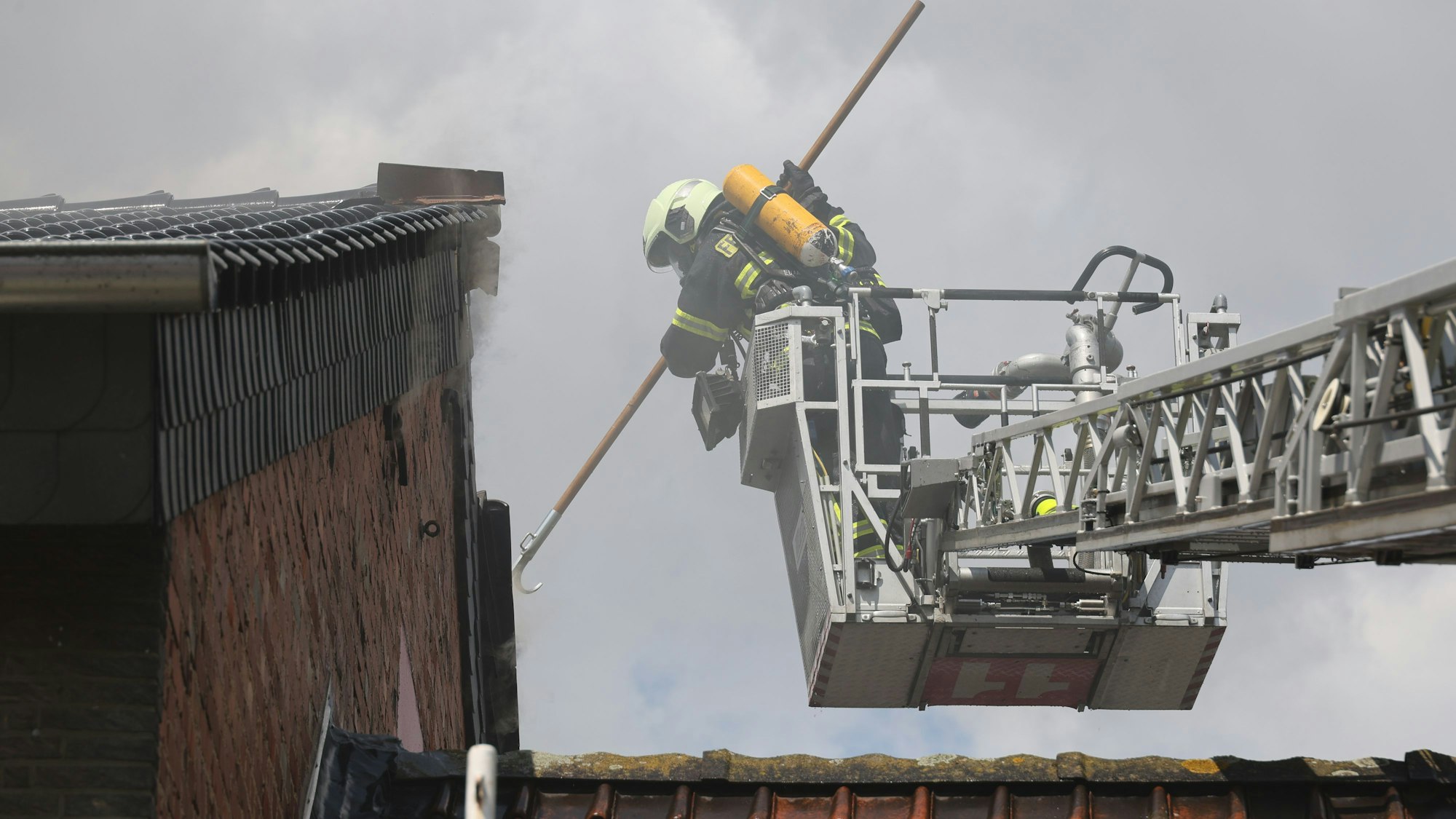 Der Feuerwehrmann, der Atemschutz trägt, stößt den Einreißhaken in die Dachziegel.