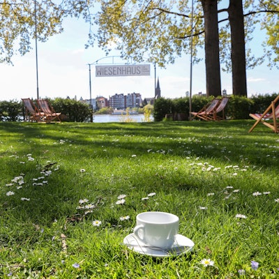 Das Café Uferglück befindet sich im Wiesenhaus, ein Gelände für Camping und Tiny Houses. Zu sehen ist die Wiese mit Liegestühlen und Blick auf den Rhein.