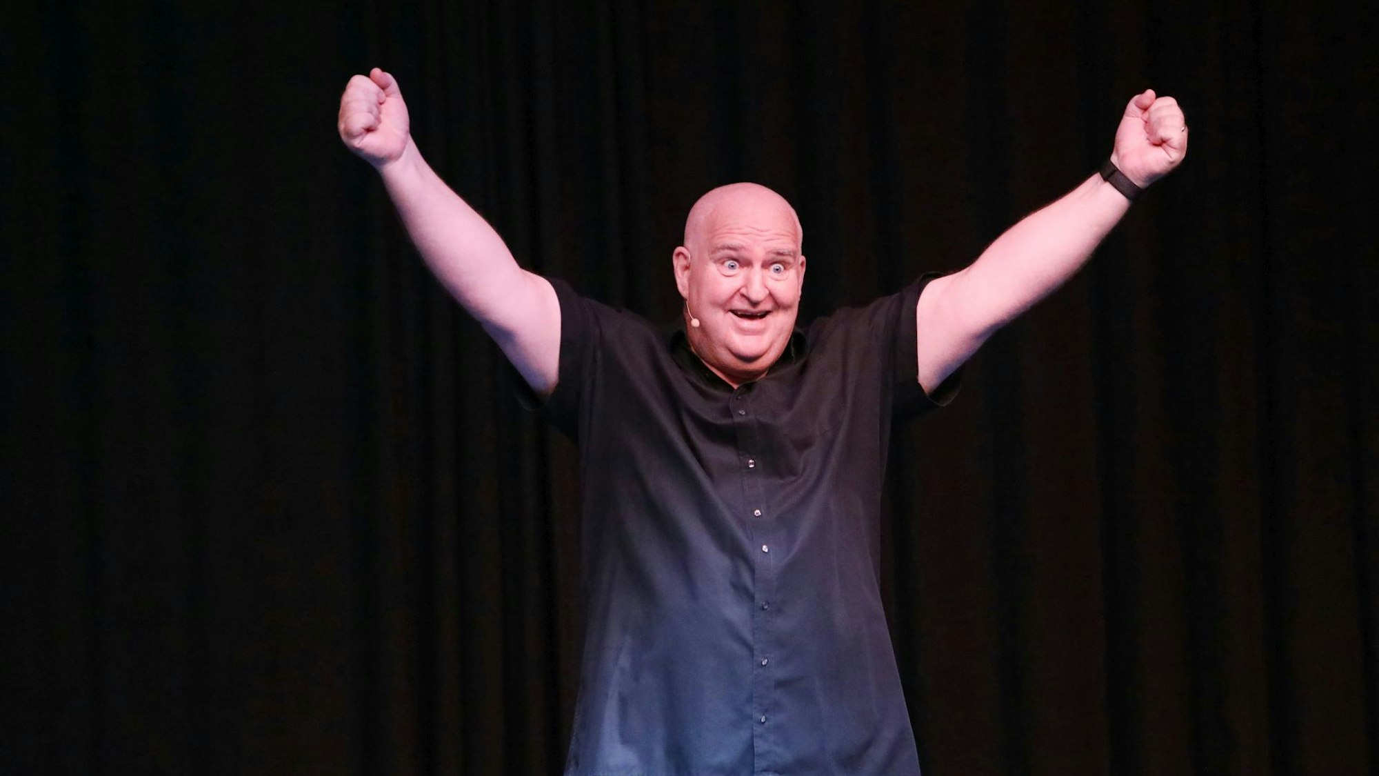 Ein Mann im schwarzen Hemd reckt beide Arme in die Höhe.