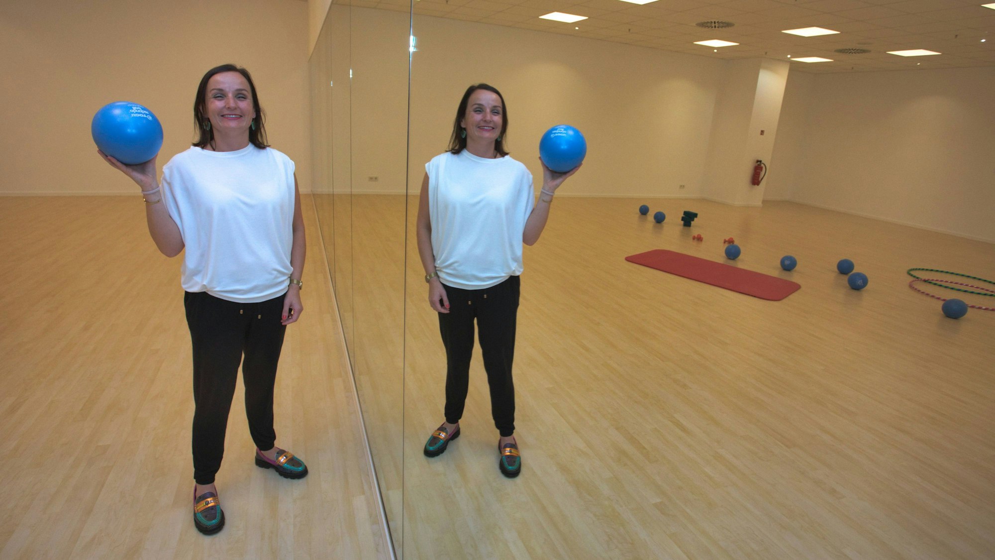 Eine Frau steht mit einem blauen Ball neben einer Spiegelwand.
