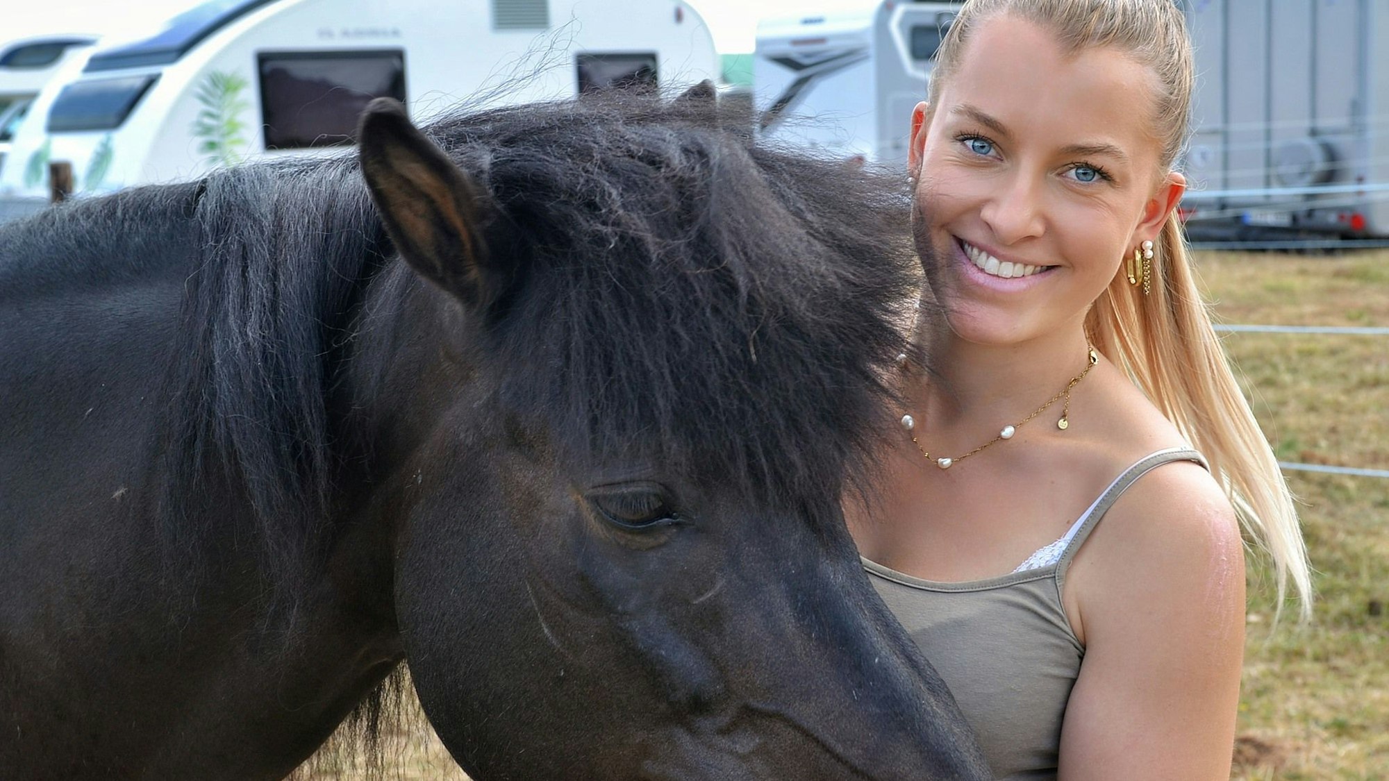 Jenna Nelles hält ihre Hand an den Kopf eines Islandpferds und lächelt dabei in Richtung der Kamera.