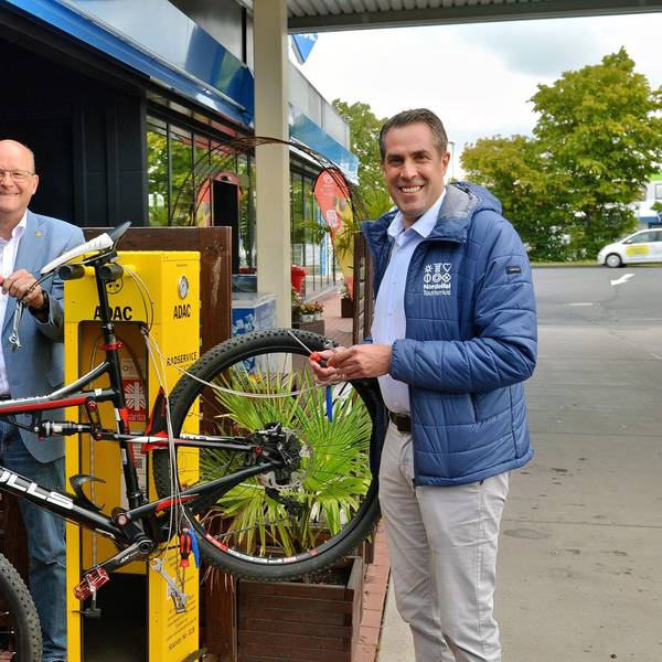 André Schiebahn (v.l.), Thomas Velling und Patrick Schmidder stehen neben der Servicestation, an der ein Fahrrad befestigt ist.