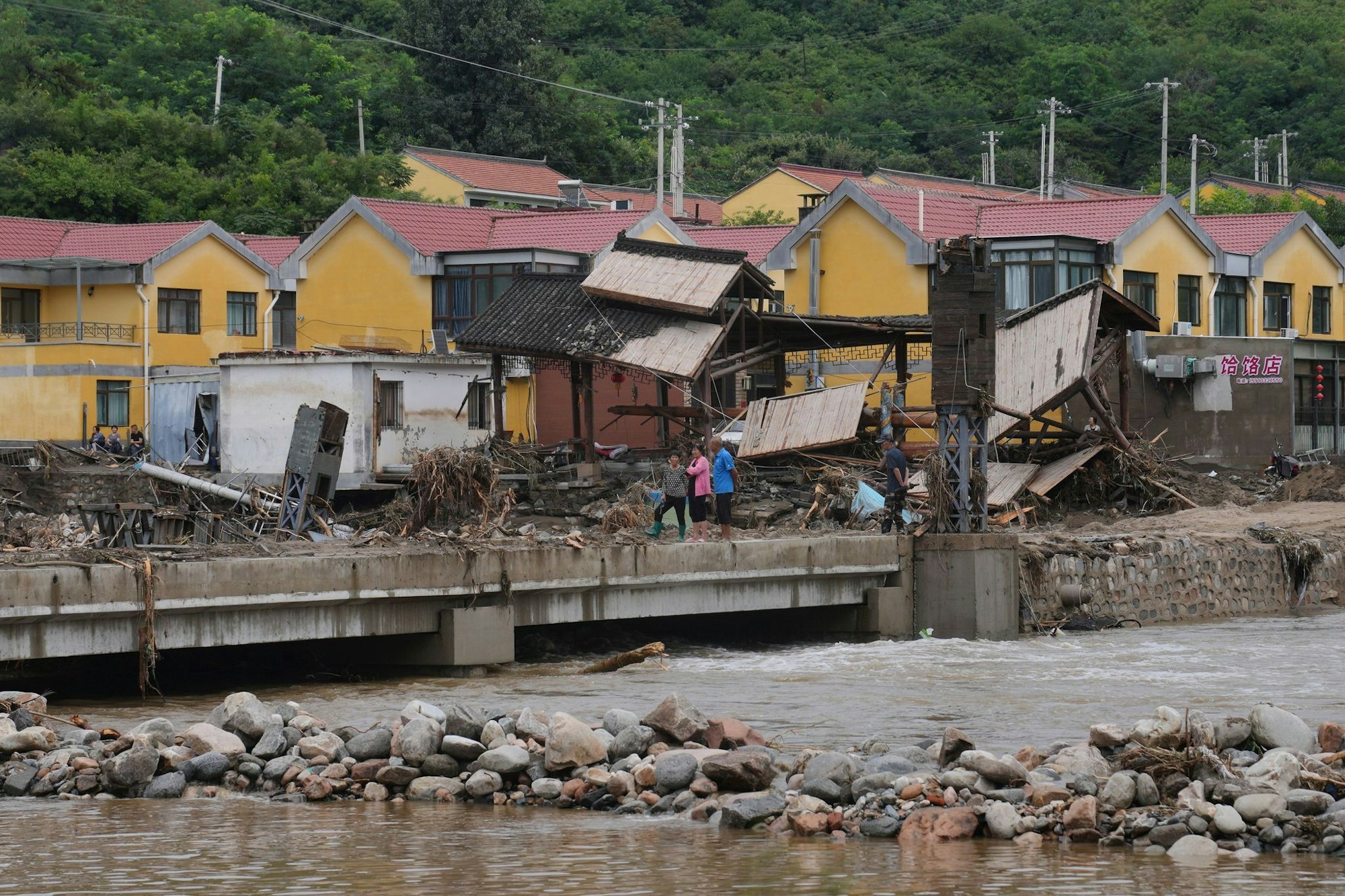 Dorfbewohner versammeln sich in der Nähe einer Brücke, die nach schweren Regenfällen im Bezirk Miyun am Stadtrand von Peking überflutet wurde.
