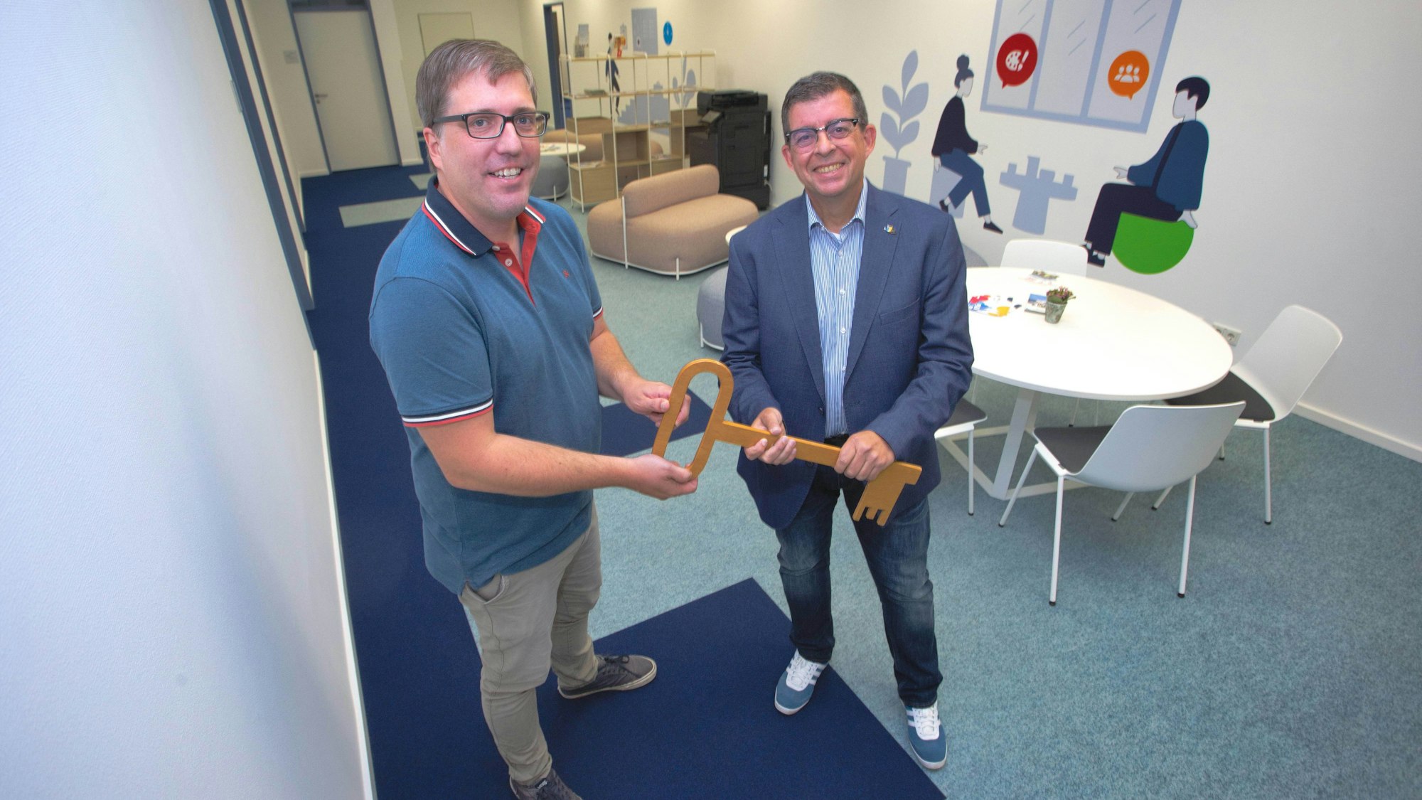 Zwei Männer stehen nebeneinander und halten einen überdimensionalen Holzschlüssel in der Hand.