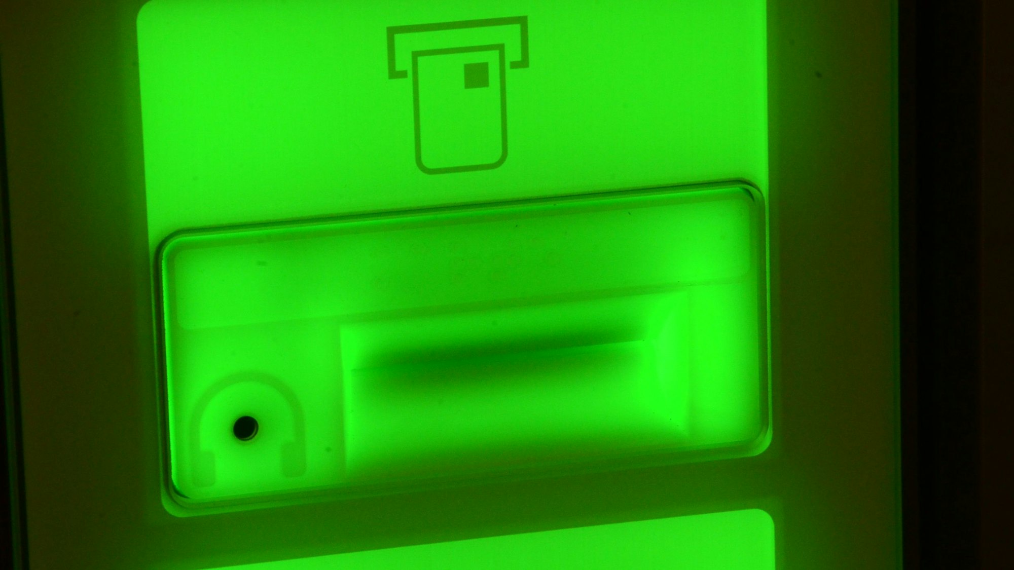 Ein grün leuchtendes Display an einem Geldautomaten. Zu sehen ist das Symbol für eine EC-Karte und das für einen Kopfhörer über dem Anschluss.