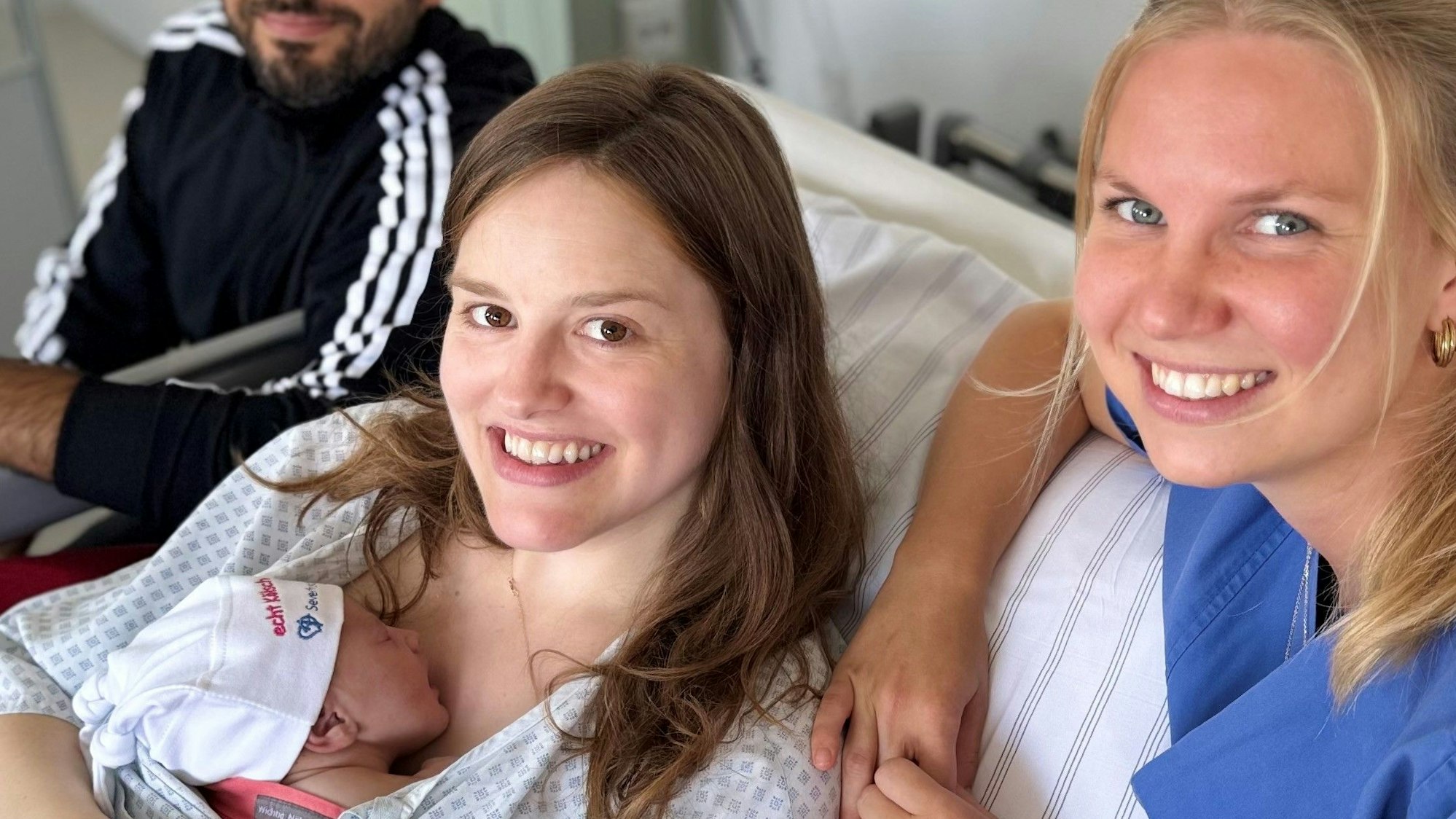 Die Eltern und Hebamme mit dem Jubiläumsbaby im Krankenhauszimmer