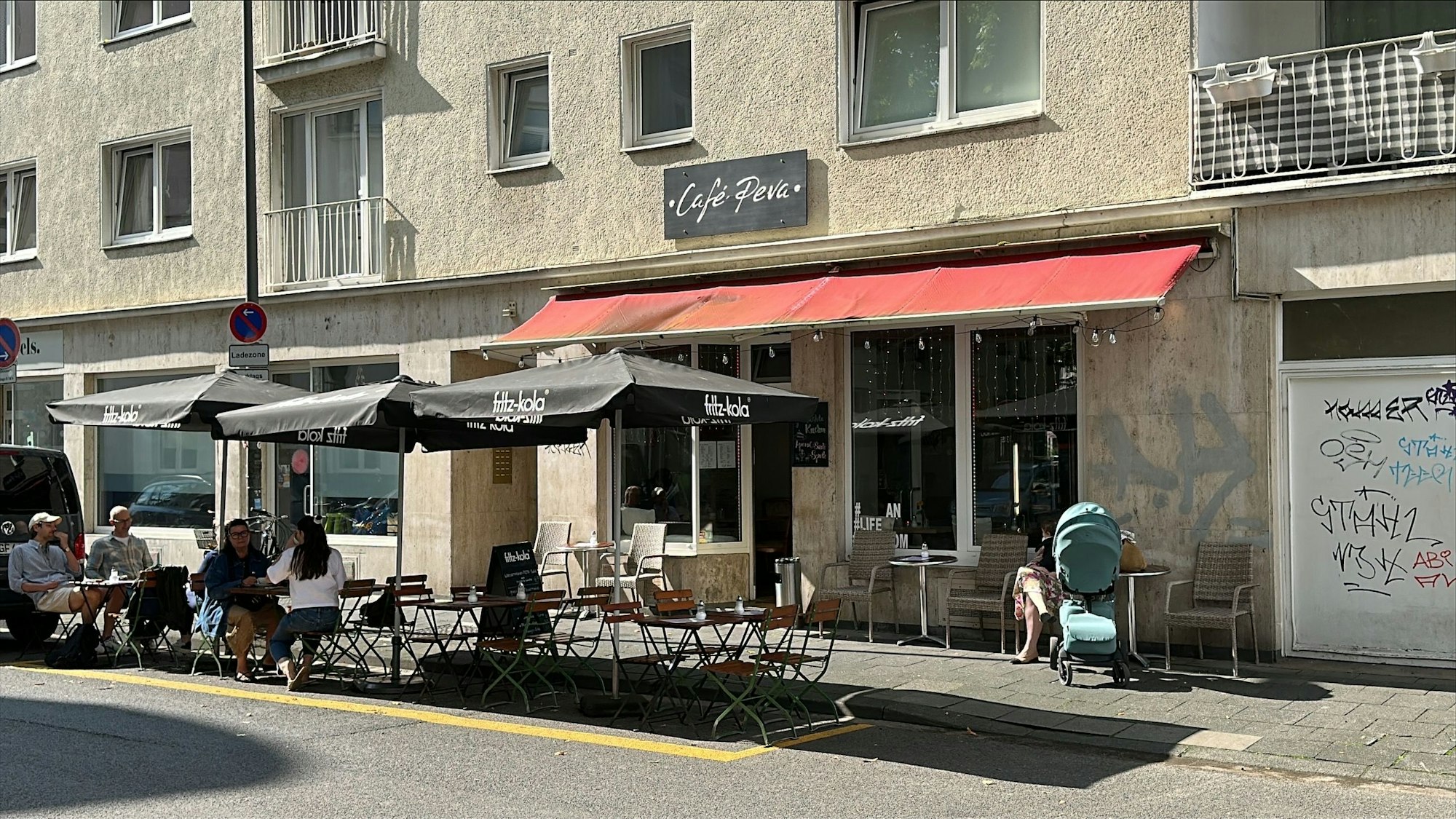 Das Café Peva in der Südstadt in Köln von außen, vor der Tür sind Sitzplätze und Tische, auf denen Gäste sitzen.
