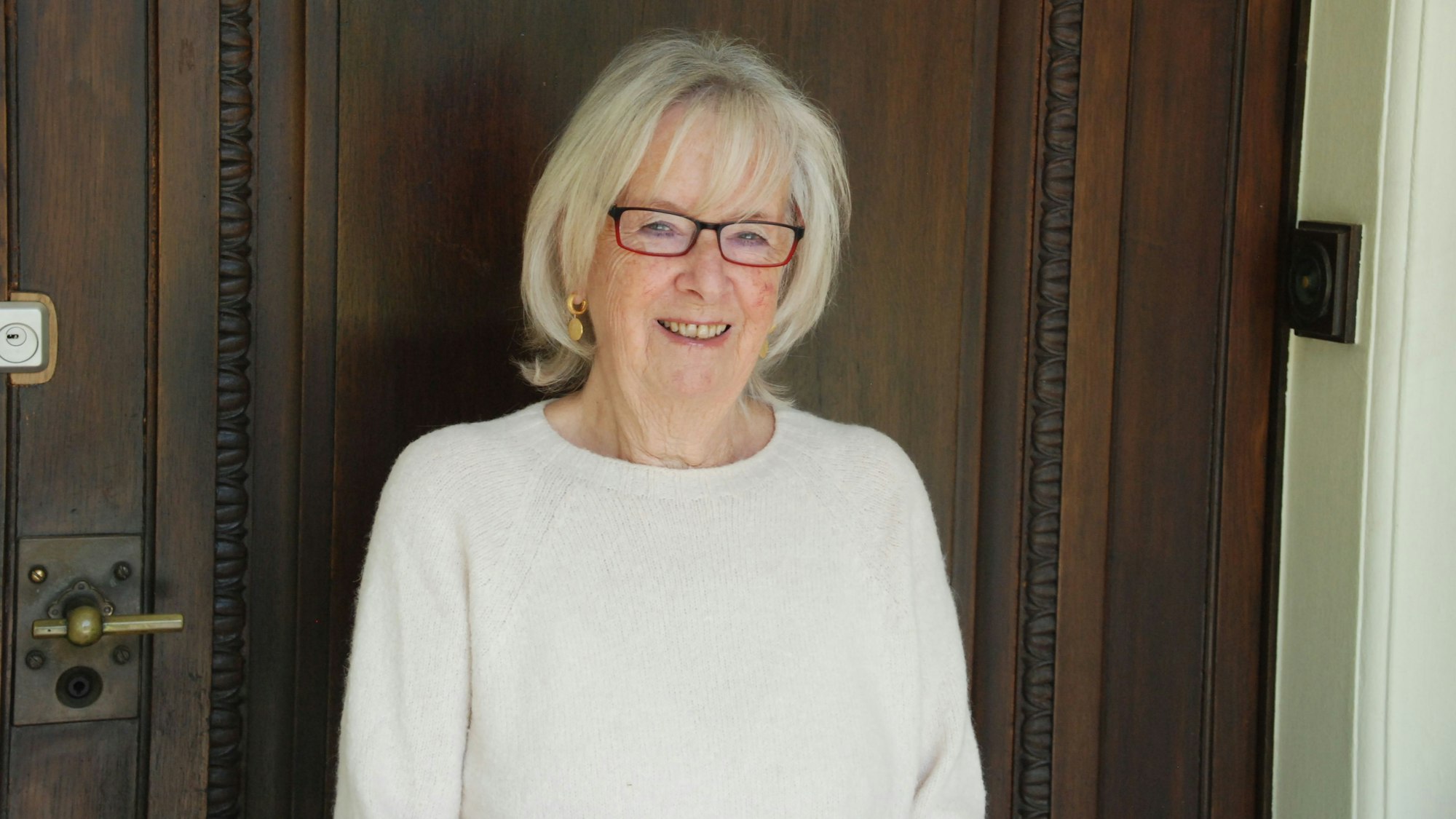 Vera von Schnitzler trägt eine Brille und lächelt vor einer verschlossenen Tür.