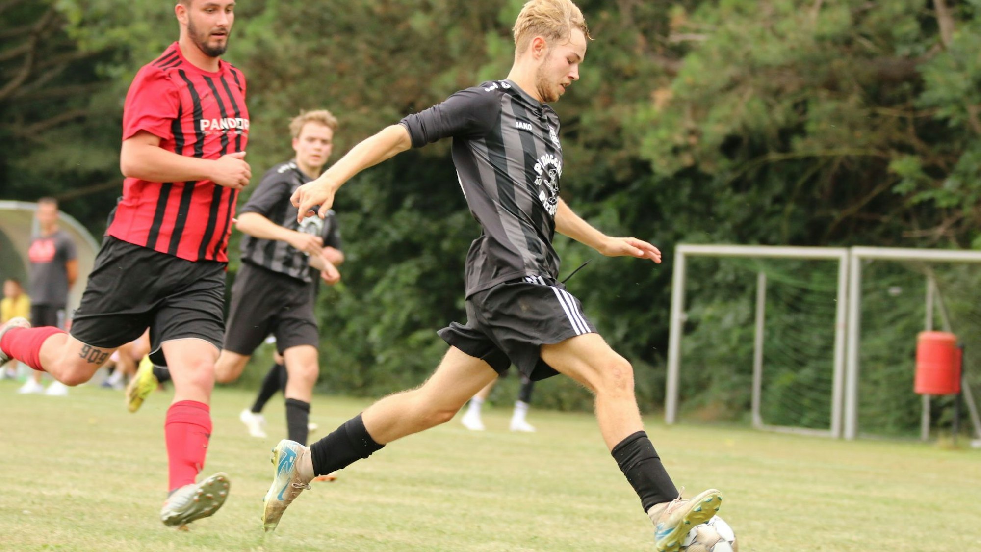 Ein ballführender Fußballer wird von einem Gegenspieler verfolgt. Zu erkennen sind die fast nicht vorhandenen Schienbeinschoner.