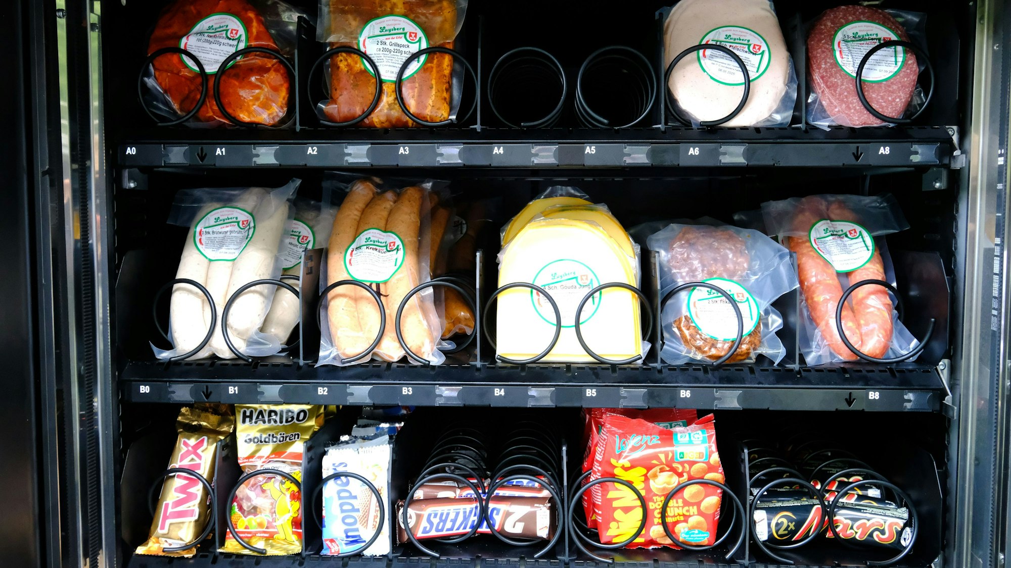 Die Detailaufnahme zeigt einen Teil des Warenangebots eines Verkaufsautomaten: Fleischprodukte wie Würstchen und Aufschnitt sowie verschiedene Süßigkeiten.