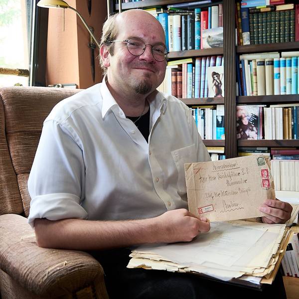 Der Autor Andreas Züll sitzt vor einem Regal voller Bücher und hält einen alten Briefumschlag in der Hand.