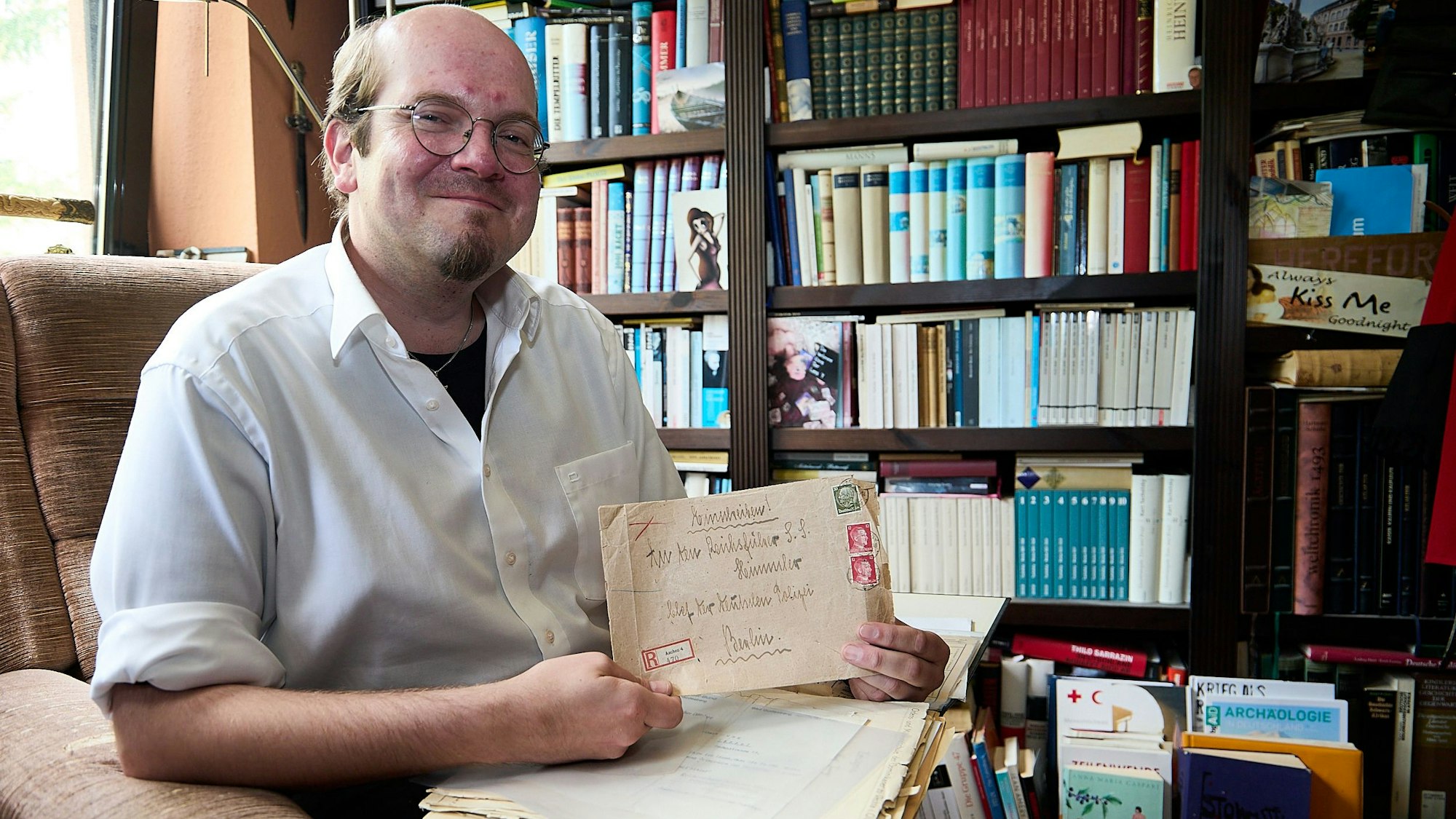 Der Autor Andreas Züll sitzt vor einem Regal voller Bücher und hält einen alten Briefumschlag in der Hand.