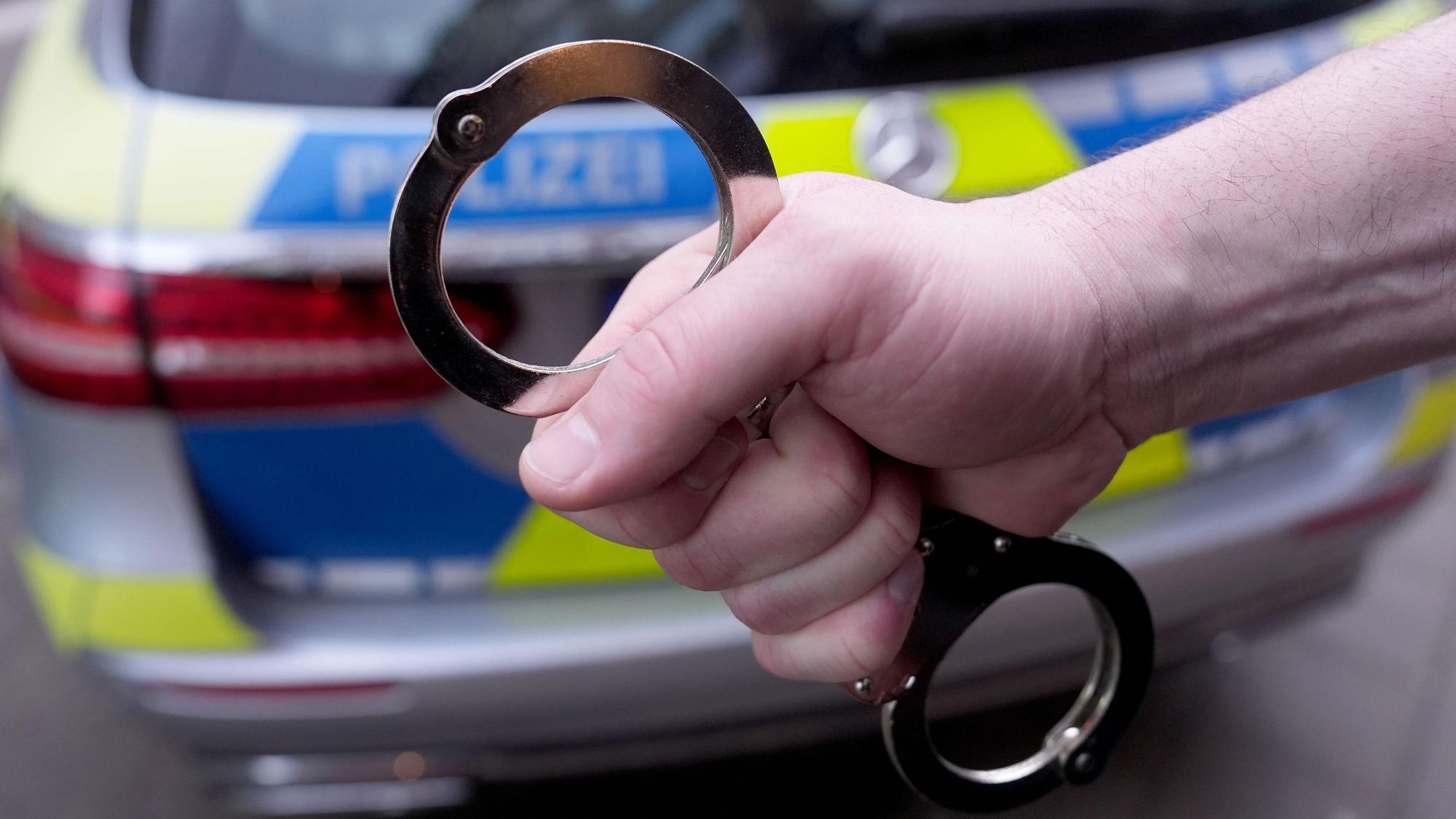 Ein Polizist hält Handschellen vor einem Einsatzfahrzeug hoch.