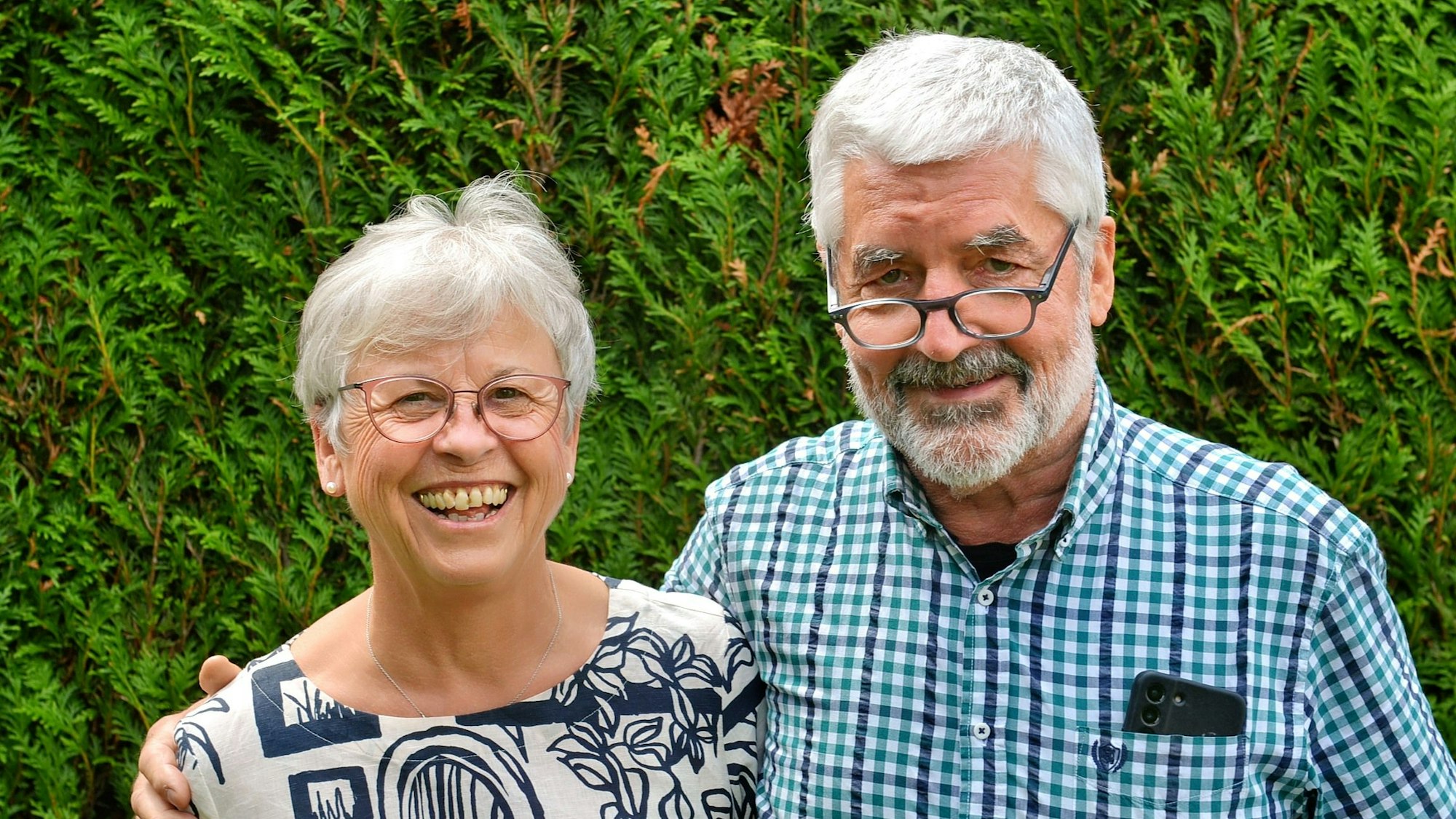Annegret und Christoph Schmitz stehen vor einer Hecke. Er hat seinen Arm um sie gelegt.