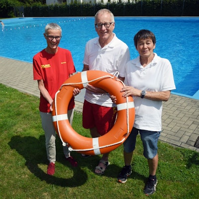 Ein Mann und zwei Frauen von der SLRG stehen am Beckenrand eines Freibades. In der Mitte alten sie gemeinsam einen Rettungsring in den Händen.