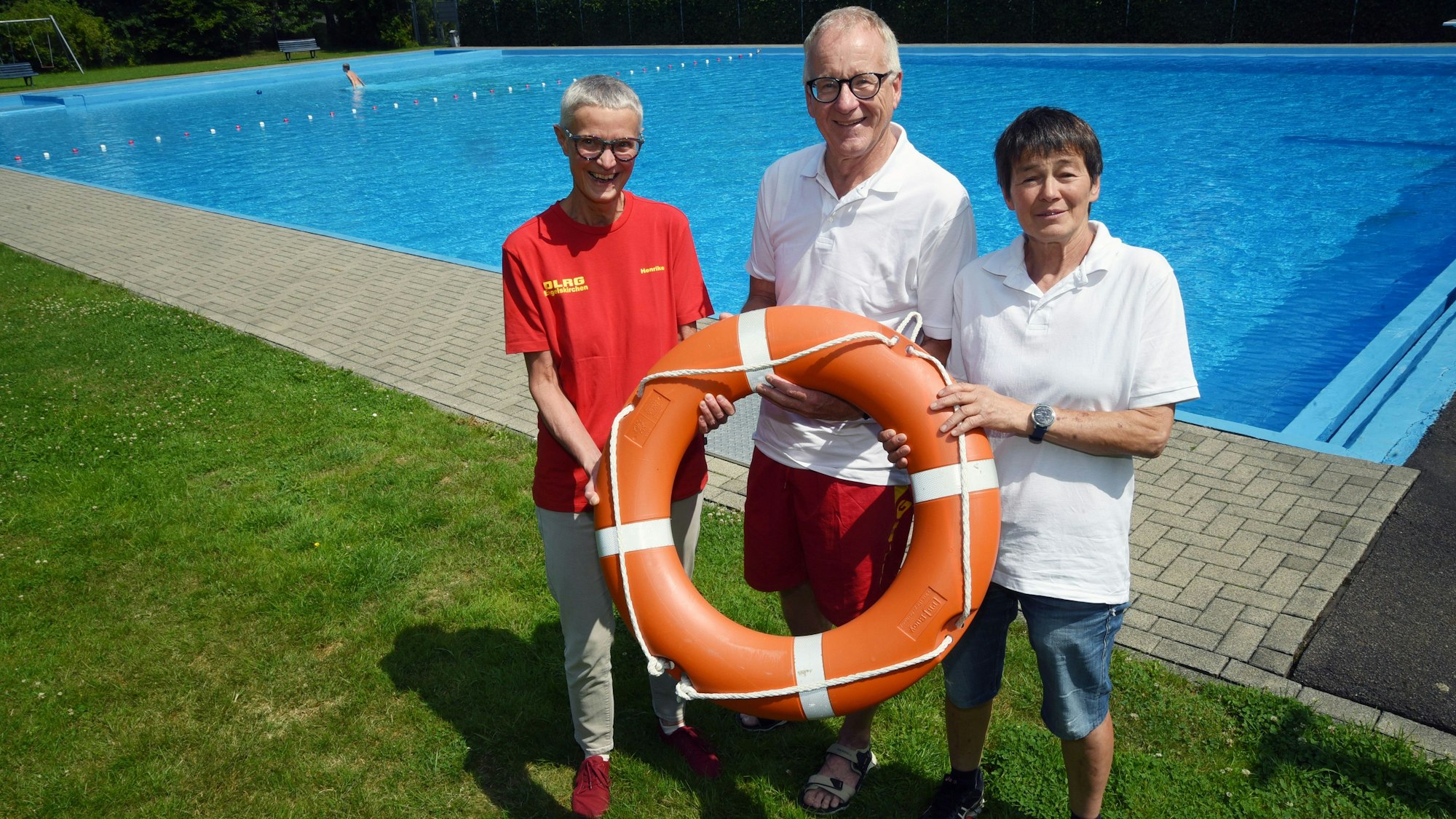 Ein Mann und zwei Frauen von der SLRG stehen am Beckenrand eines Freibades. In der Mitte alten sie gemeinsam einen Rettungsring in den Händen.