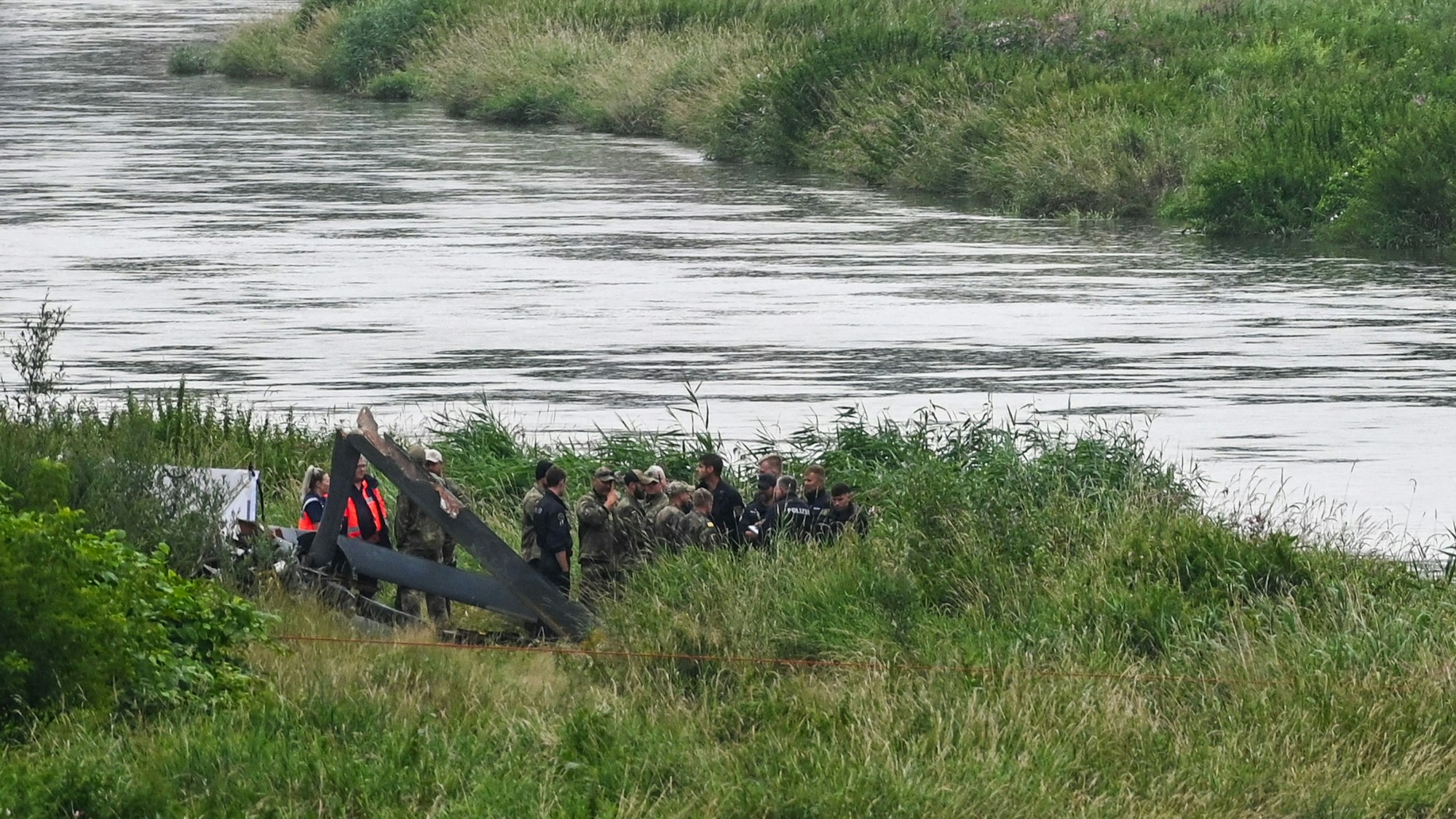 30.07.2025, Sachsen, Bahren: Bundeswehrangehörige, Polizisten und Rettungsstelle sind an der Unglücksstelle am Fluss Mulde im Einsatz. Teile des abgestürzten Hubschraubers wurden in der Nacht geborgen und an Land gebracht. Der Hubschrauber war auf einem Übungsflug der Bundeswehr abgestürzt. Foto: Heiko Rebsch/dpa +++ dpa-Bildfunk +++